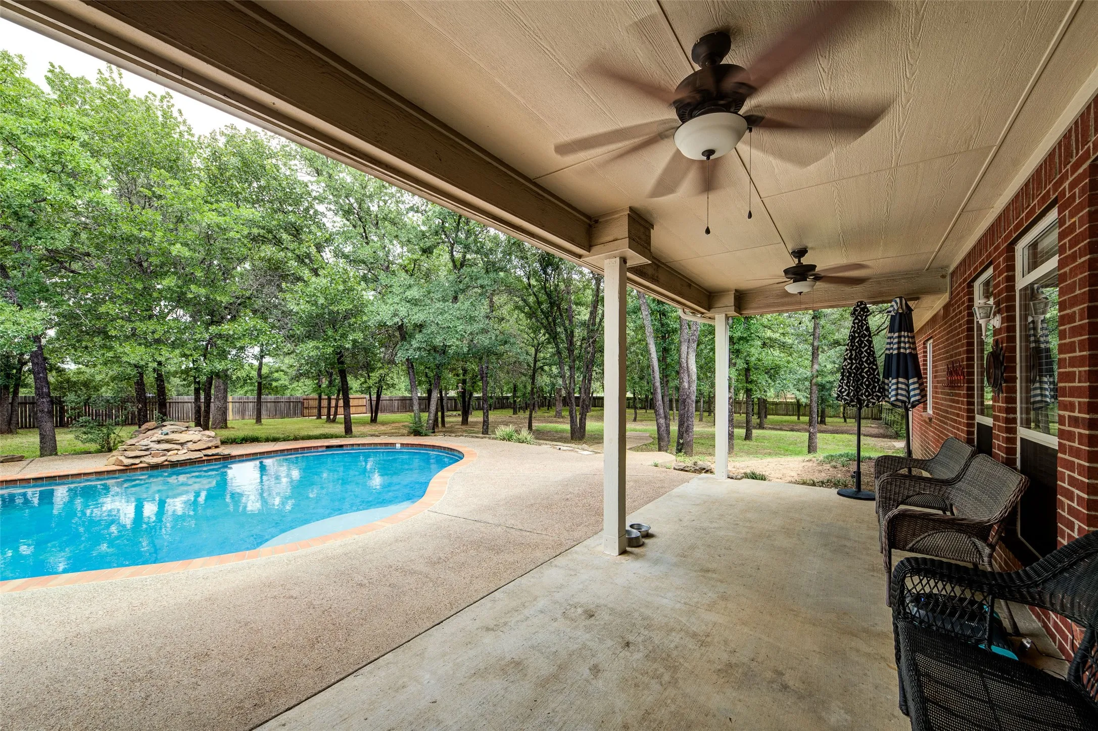 Covered patio featuring two ceiling fans, a concrete surface, and direct access to a swimming pool with a rock water feature