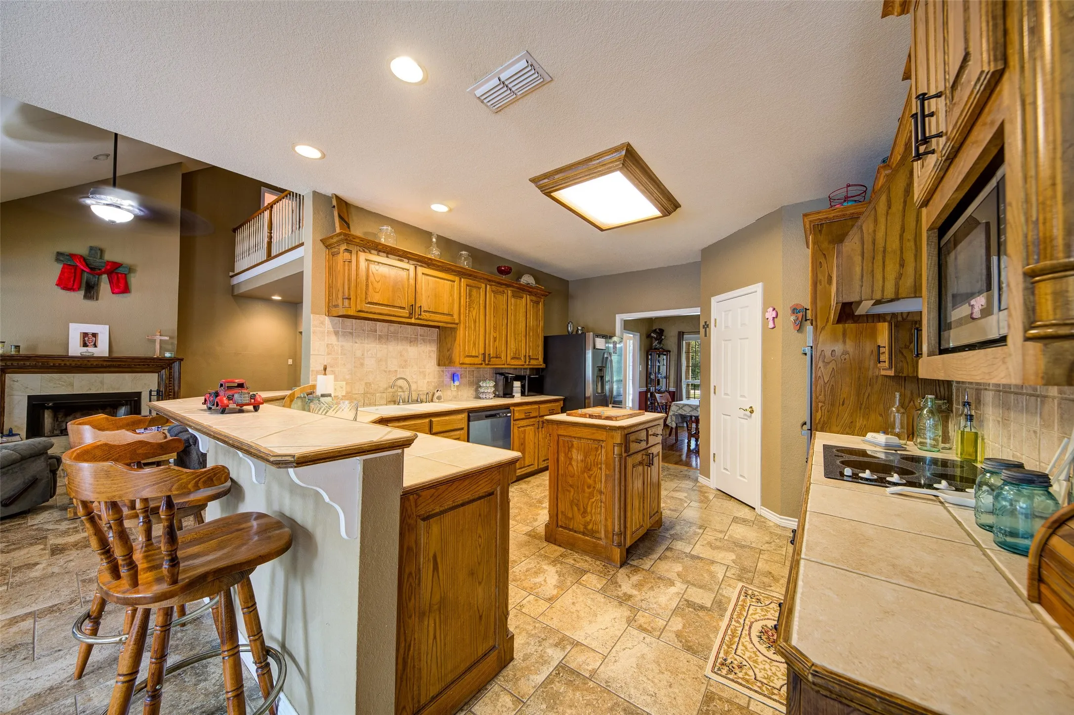 Kitchen featuring wood cabinetry, tile flooring, stone-look countertops, an island, and a built-in cooktop