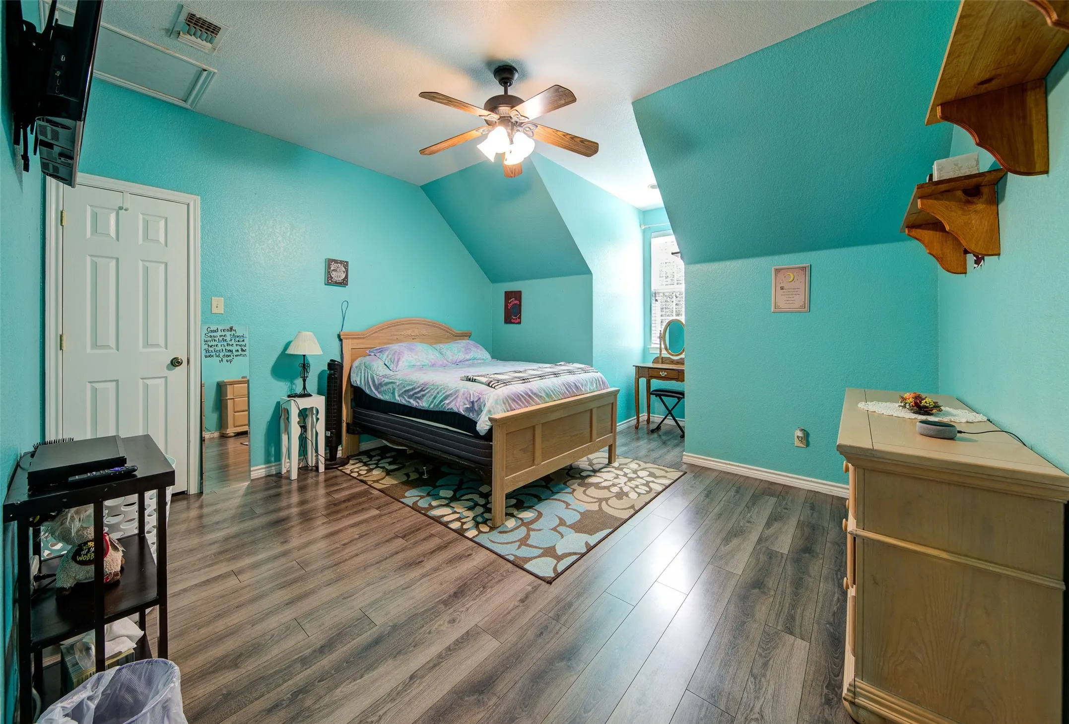 Bedroom featuring wood-finish flooring, a white paneled door, sloped ceilings, a ceiling fan with integrated lighting, and a window providing natural light
