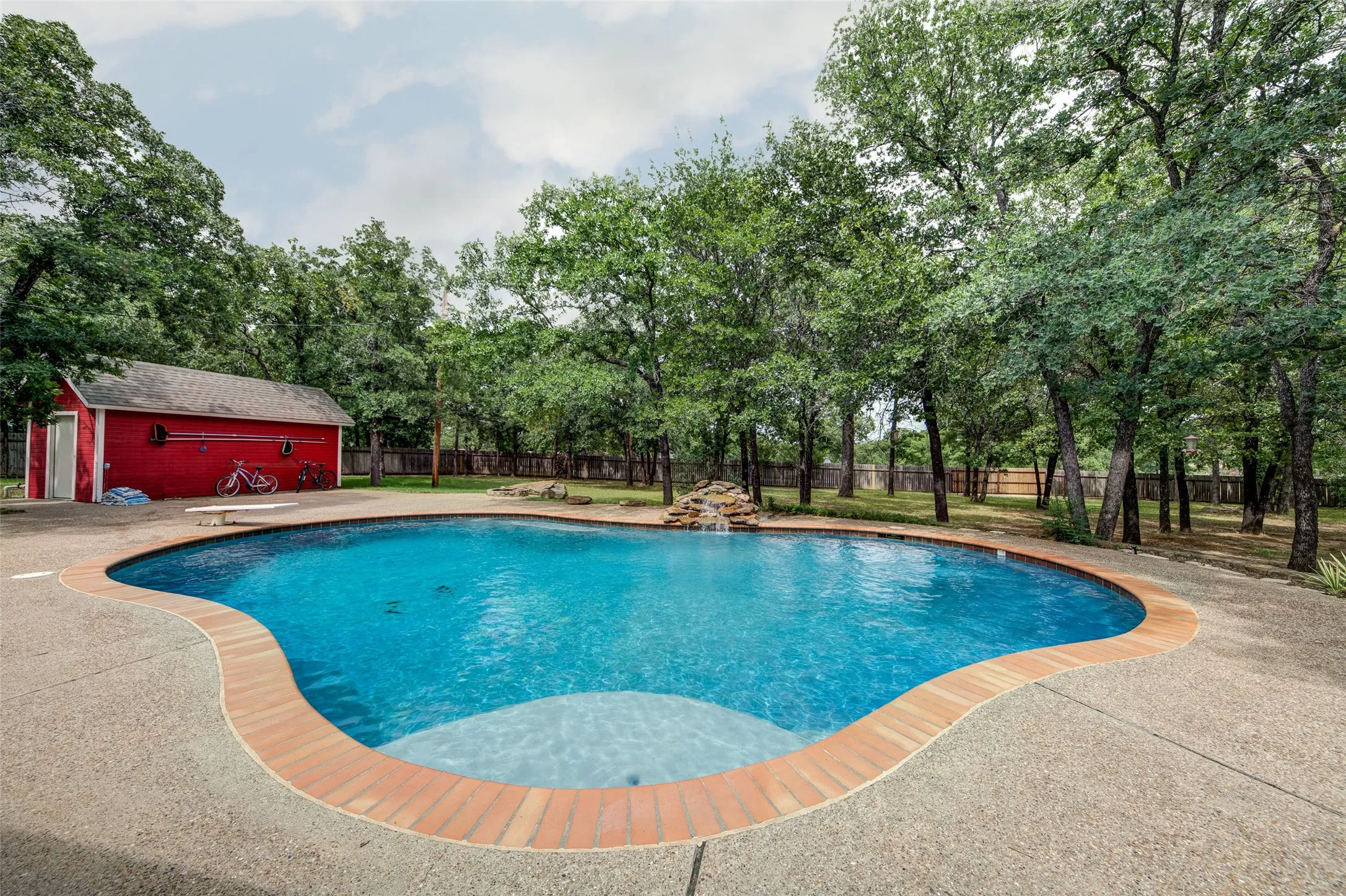 Freeform swimming pool with a brick coping, surrounded by an exposed aggregate deck