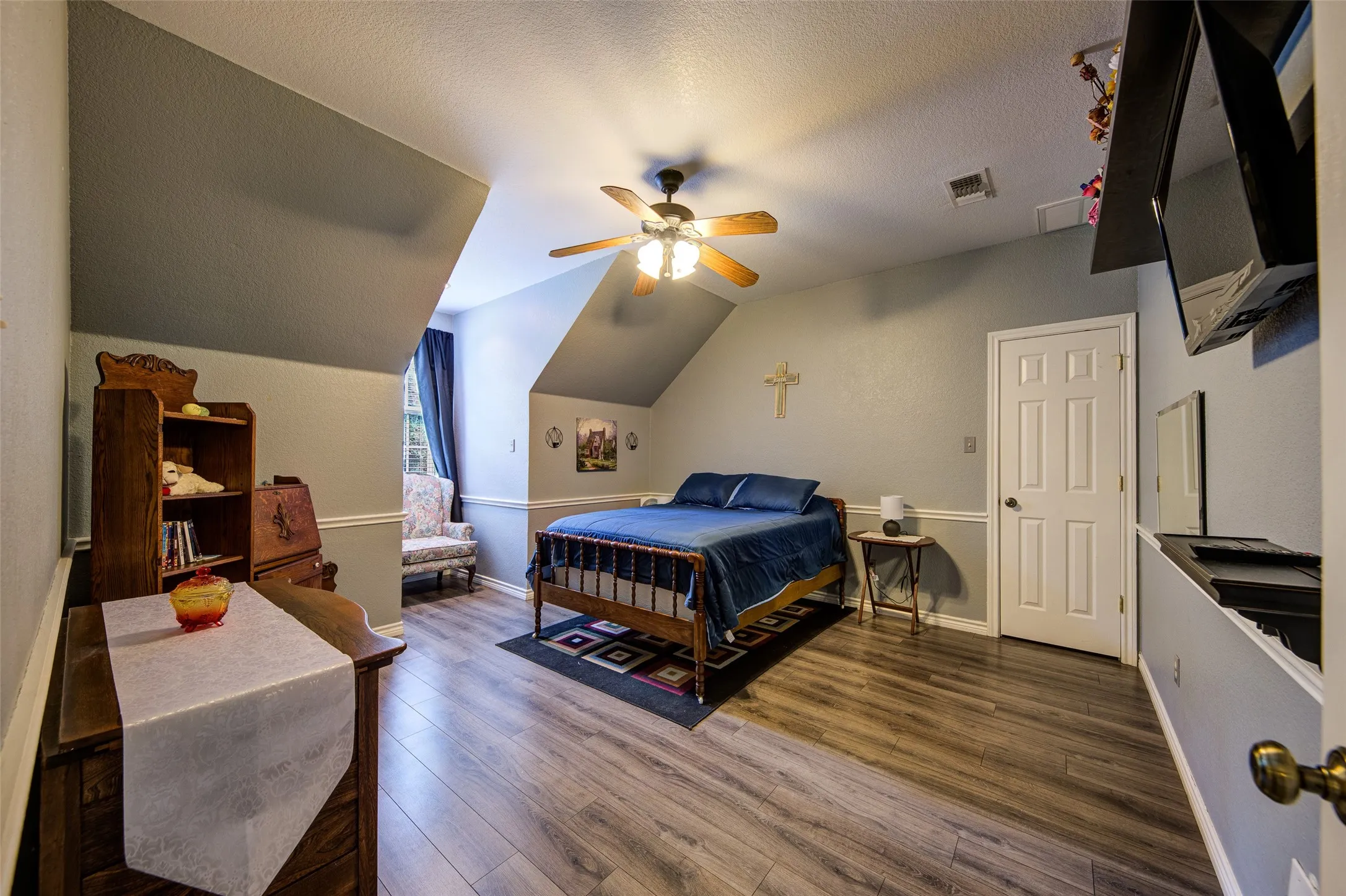 Room featuring wood-finish flooring, a ceiling fan with integrated lighting, a white six-panel door, and sloped ceiling architectural details