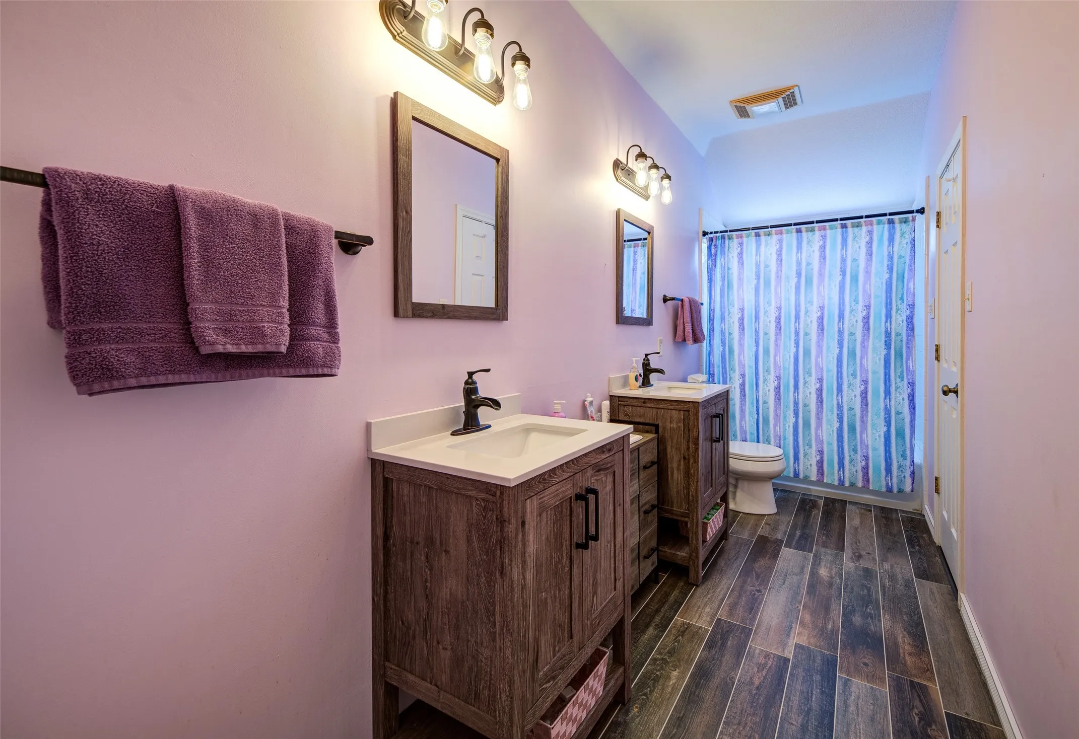 Bathroom featuring dual wood-finish vanities with undermount sinks and dark bronze fixtures, wood-finish flooring, and a shower with a privacy curtain