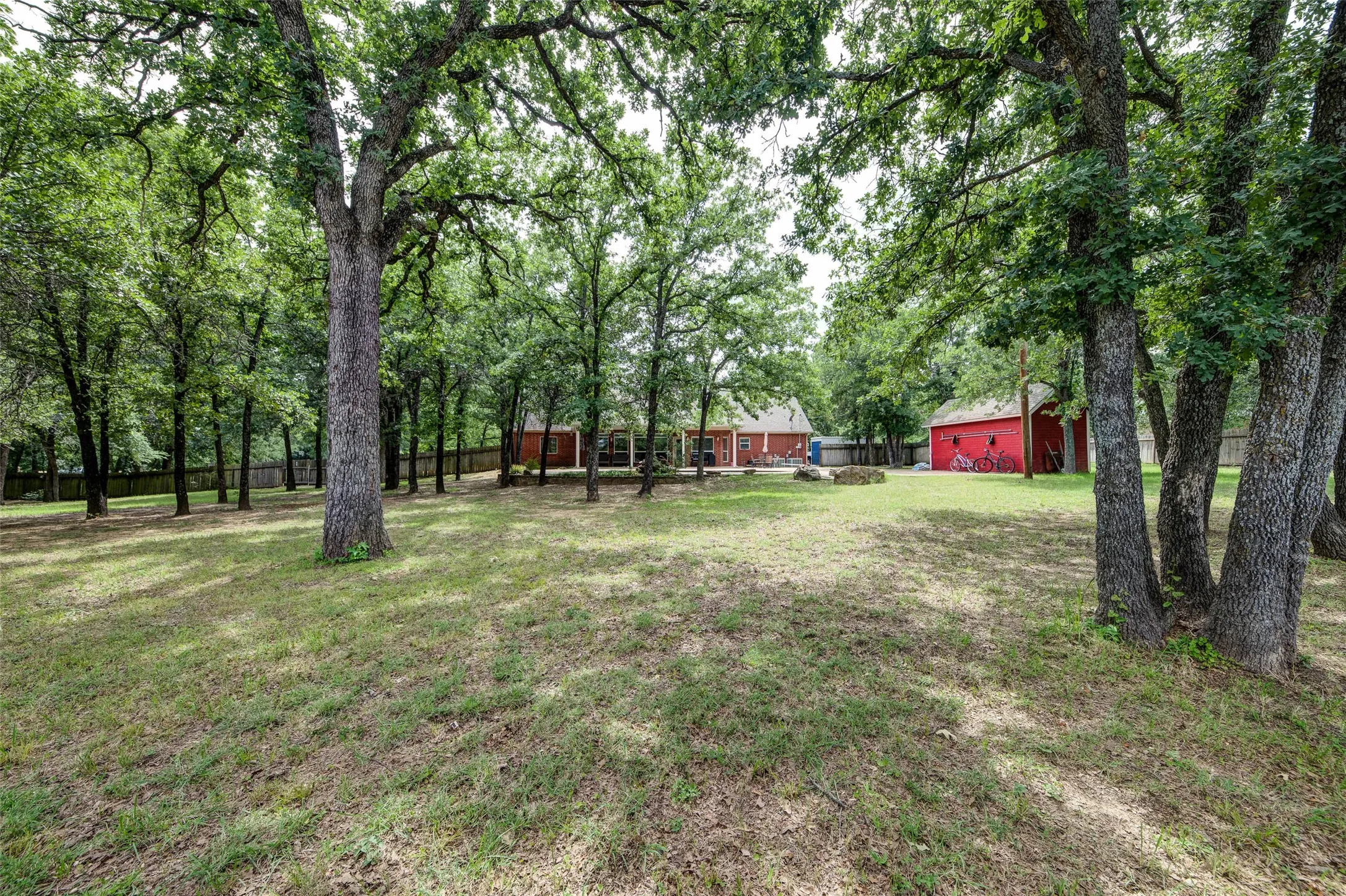 Expansive grassy yard featuring numerous mature trees, a red detached garage, and a single-story residence with a covered patio