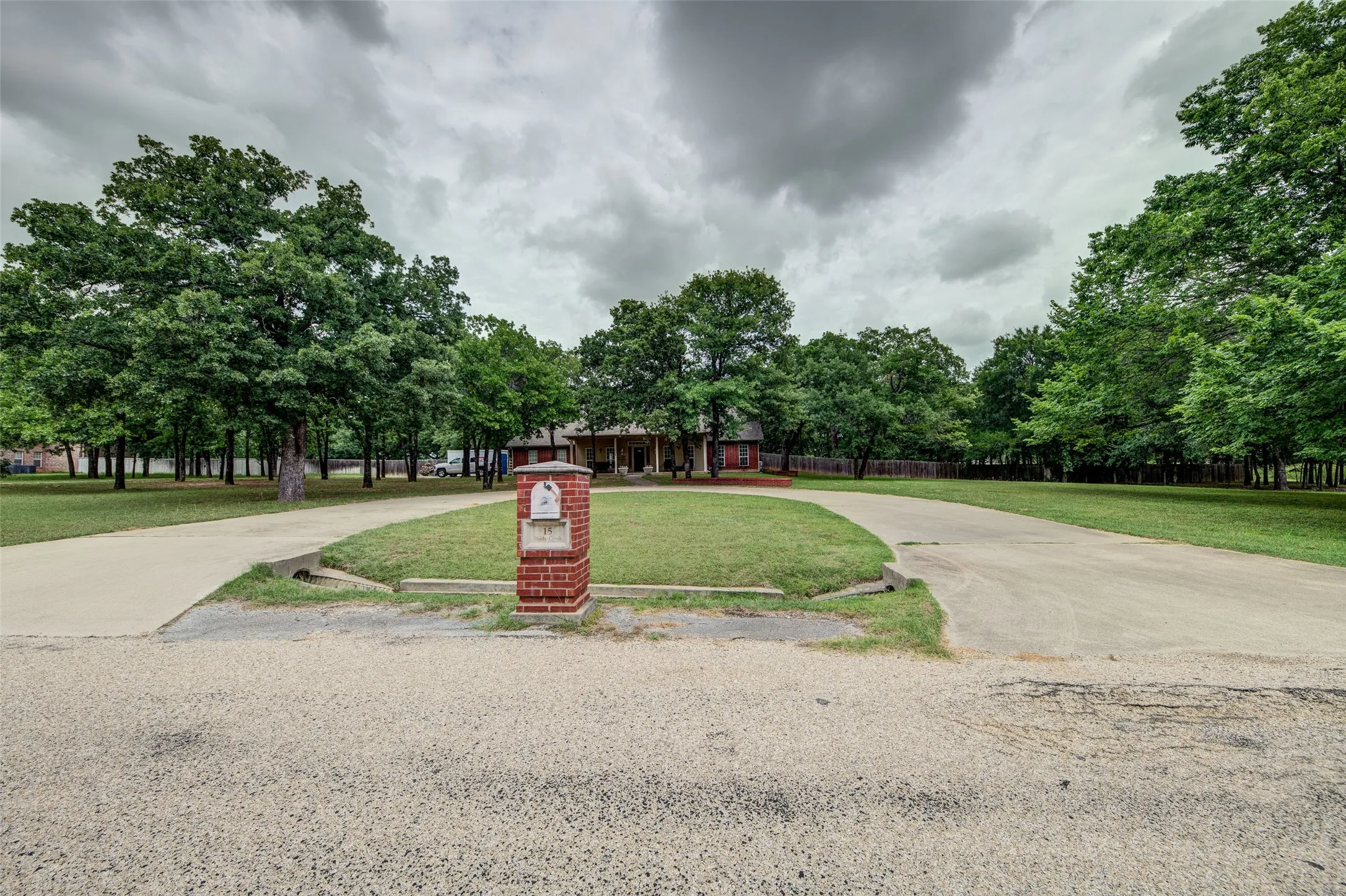 Circular concrete driveway with a central brick mailbox pillar, surrounded by mature trees and manicured lawns