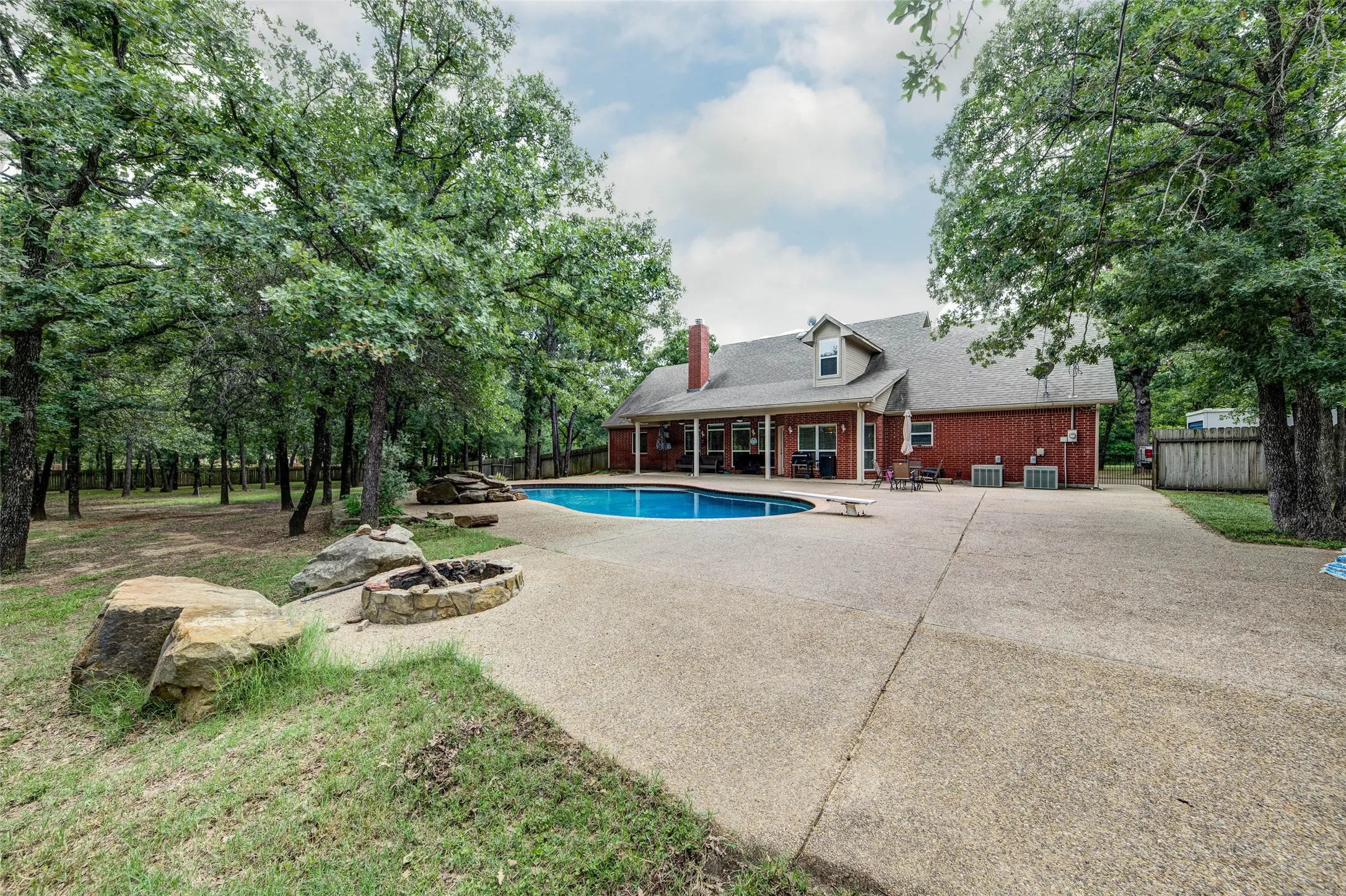 Expansive rear exterior featuring a substantial in-ground swimming pool, a built-in stone fire pit, and a wide concrete patio