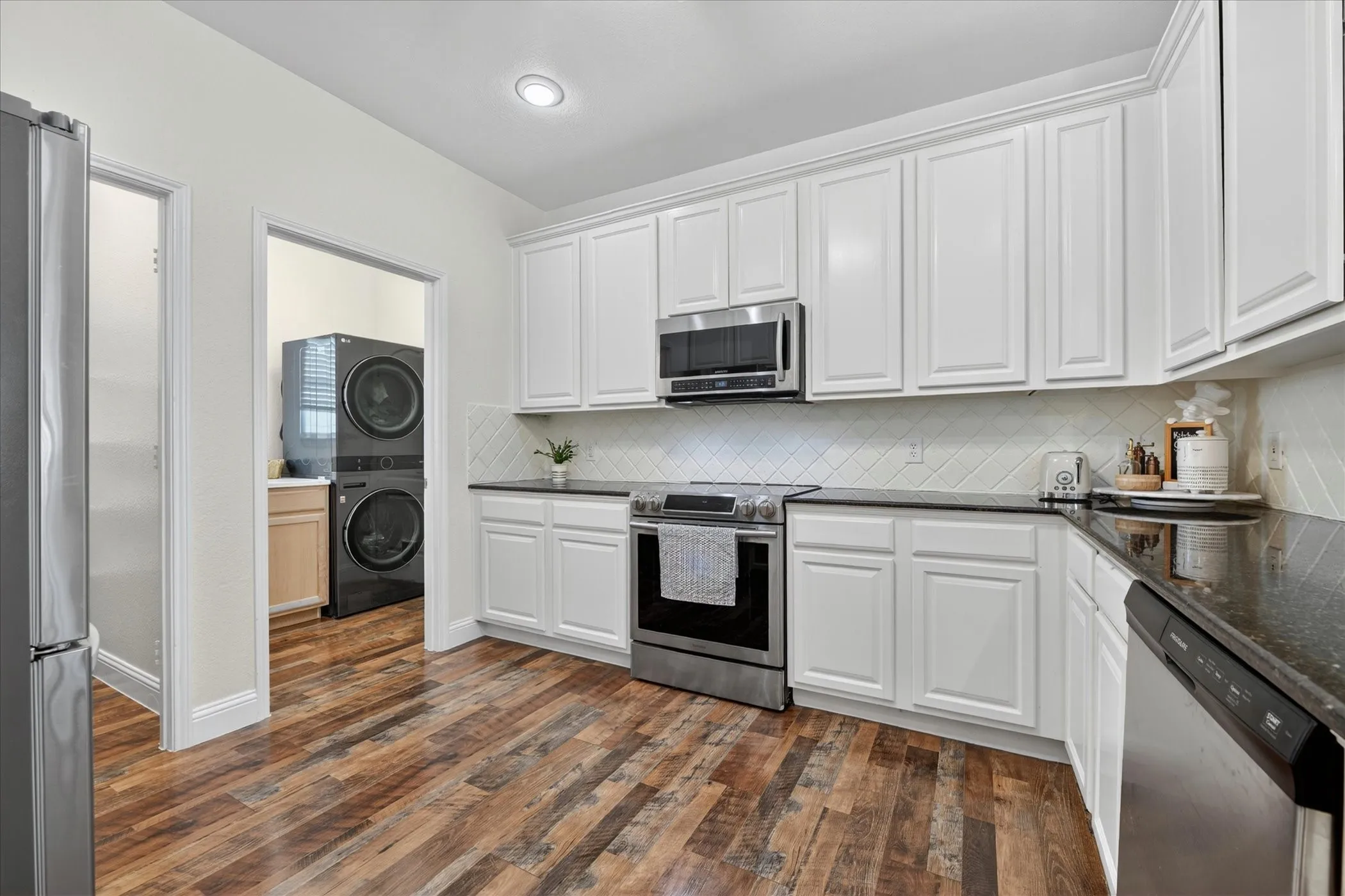 Kitchen featuring wood-finish flooring, white cabinetry, dark countertops, and stainless steel appliances