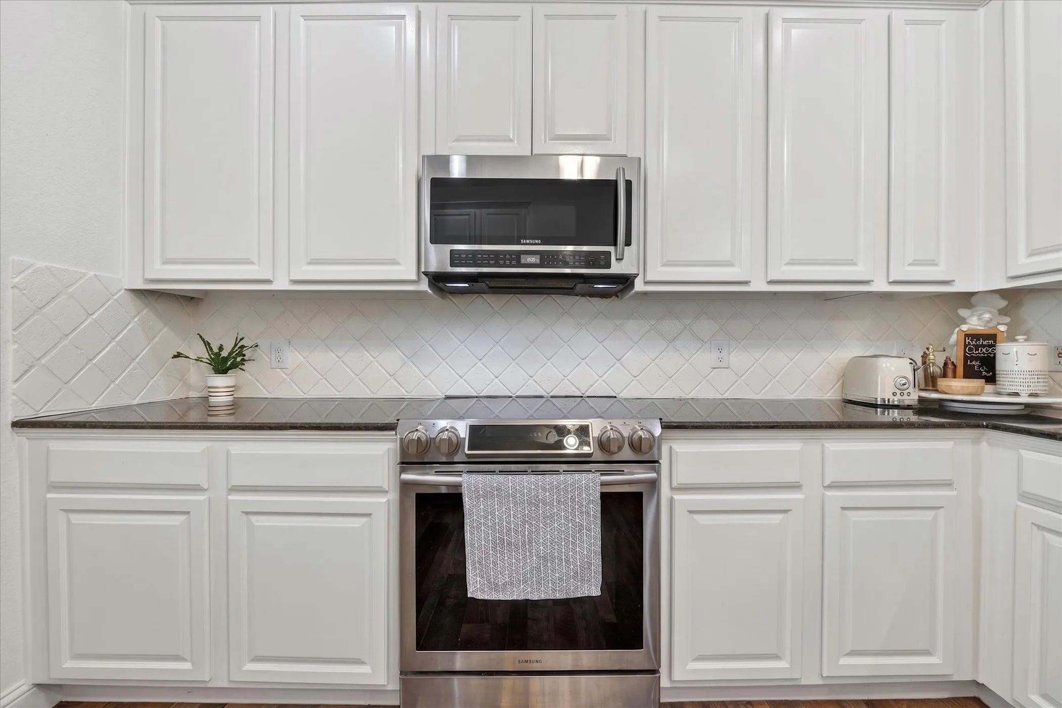 Contemporary kitchen featuring white cabinetry, dark countertops, a stainless steel range, and a microwave oven
