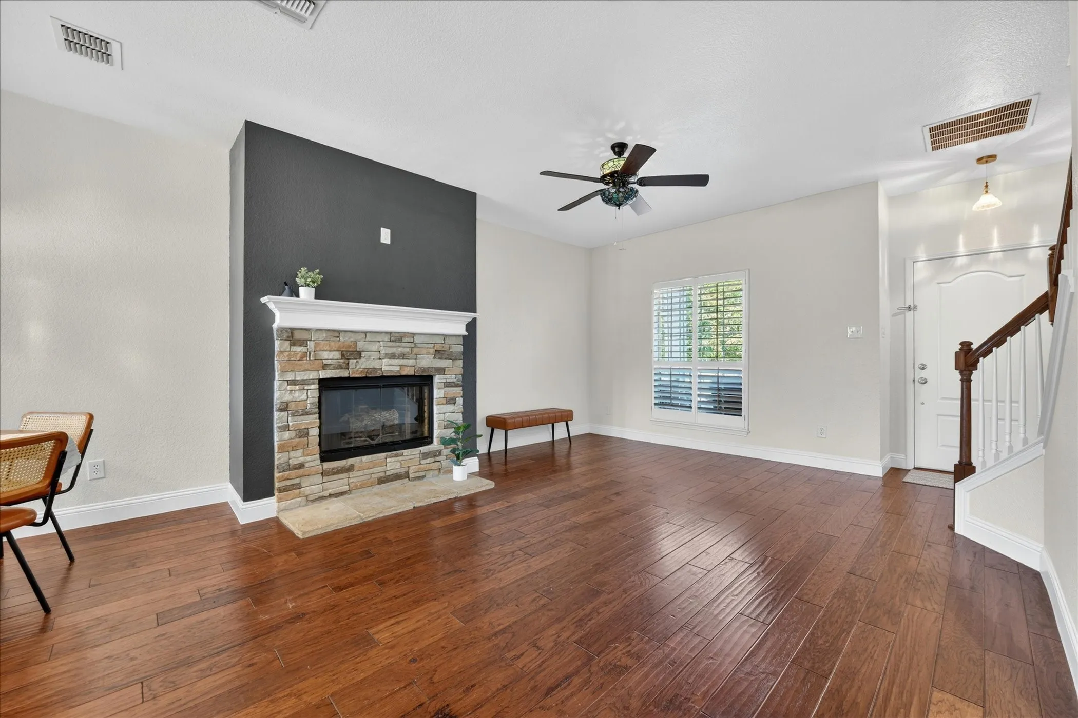 Living area featuring wood-finish flooring, a stacked stone fireplace with a white mantel, and a ceiling fan