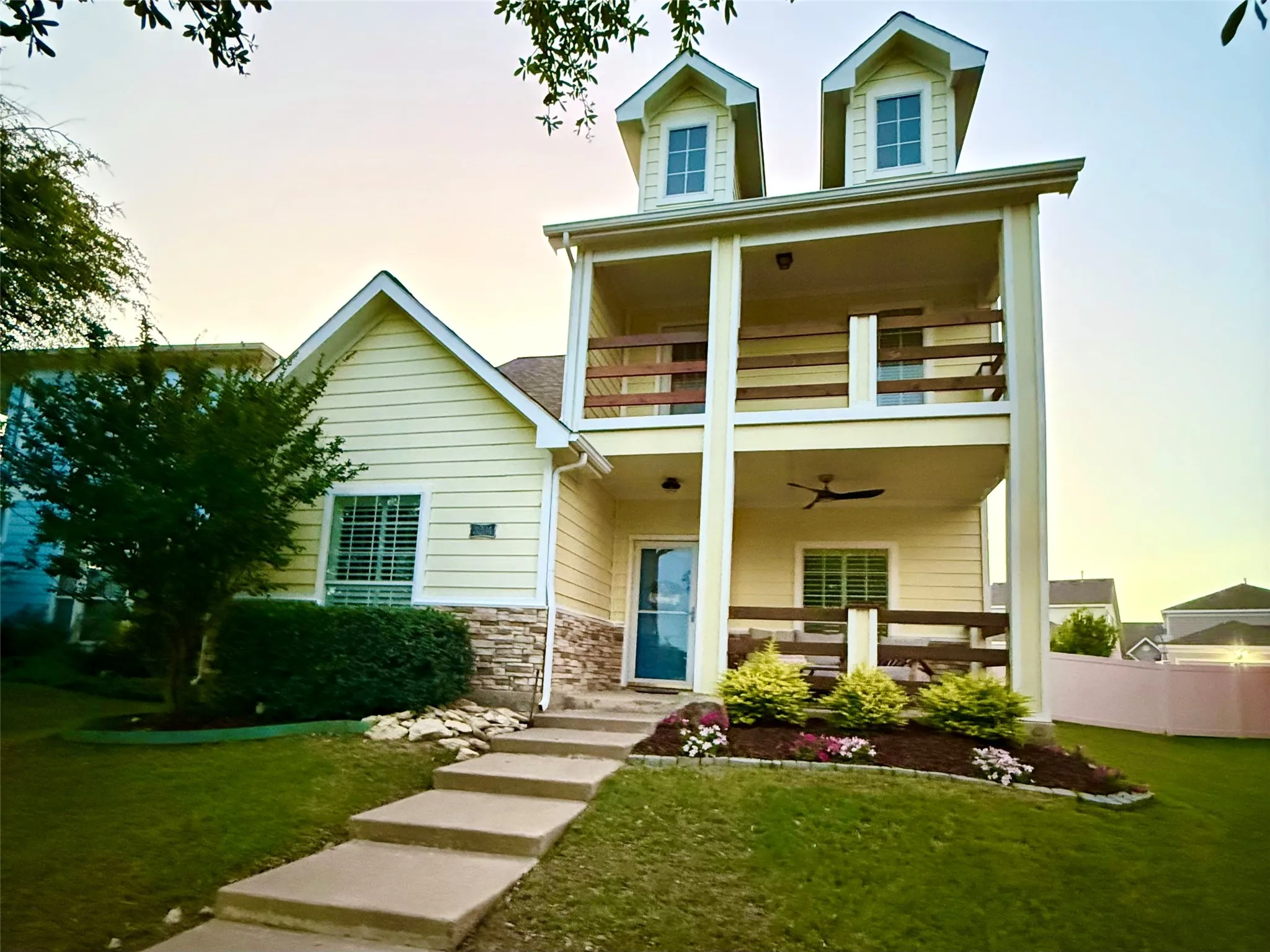 Yellow siding exterior featuring a covered porch, upper-level balcony, and two dormer windows