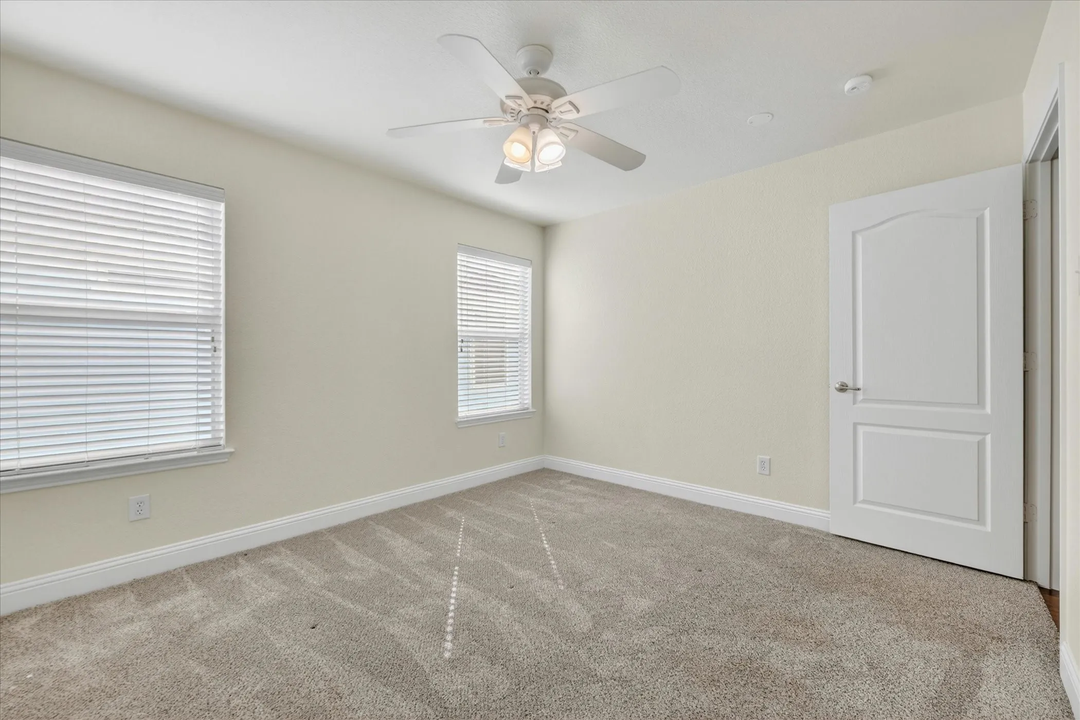 Bedroom Three Carpeted room featuring two windows with blinds, a ceiling fan with integrated lighting, and a paneled interior door