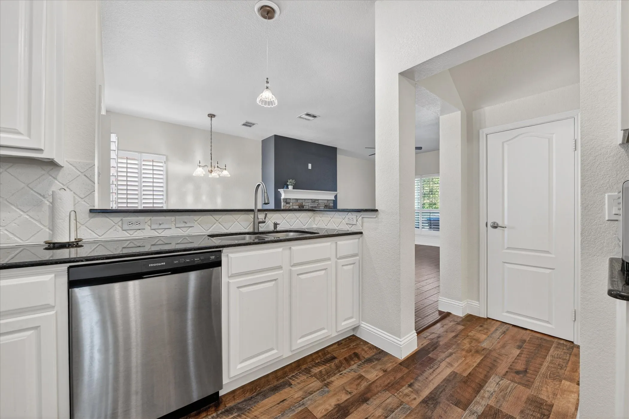 Kitchen featuring white cabinetry, a stainless steel dishwasher, black countertops, and a white diagonal-patterned tile backsplash
