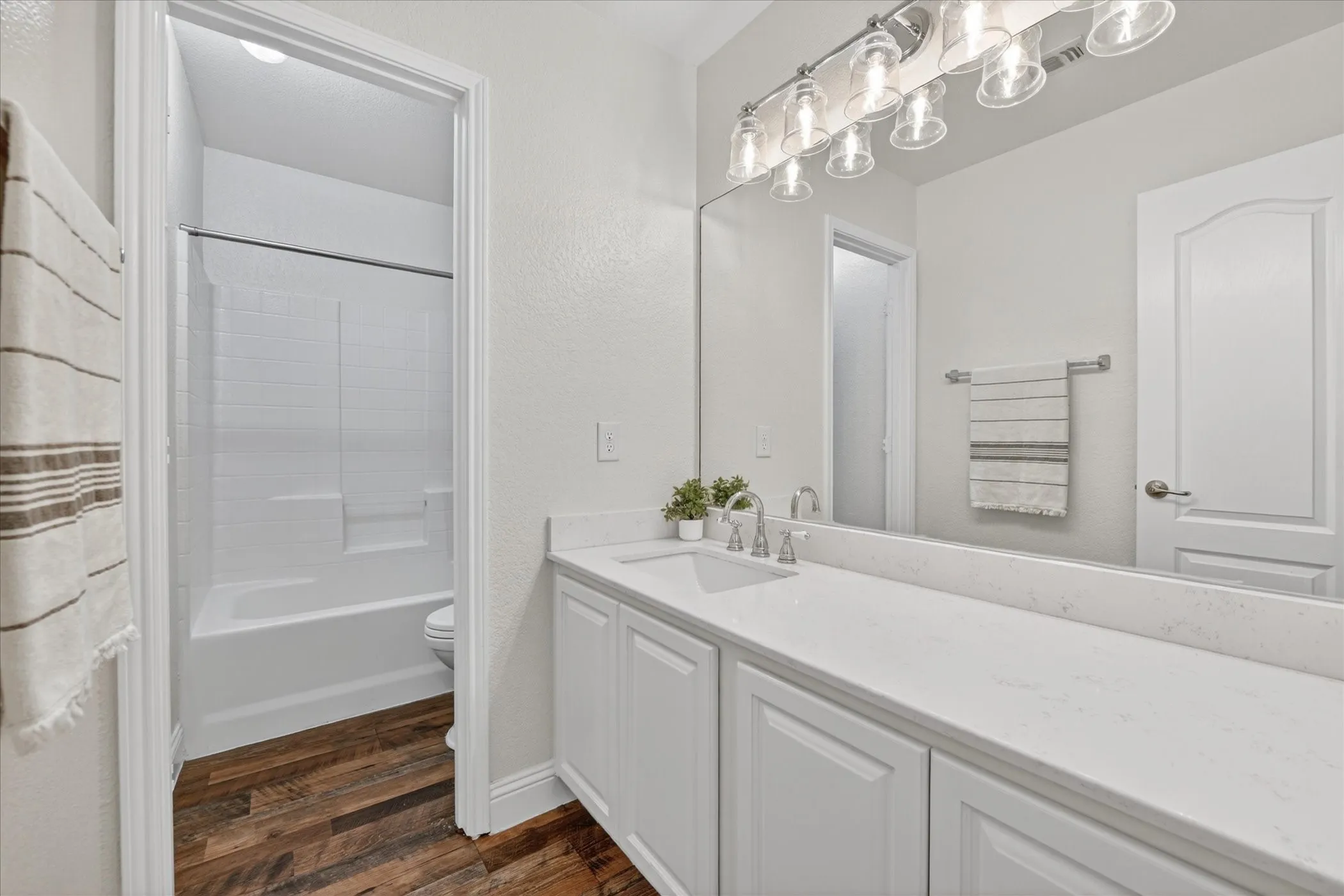 Spacious upstairs bathroom featuring a single vanity with a white countertop and base cabinetry, wood-finish flooring, a full-width mirror, and a tub/shower combination with white subway tile