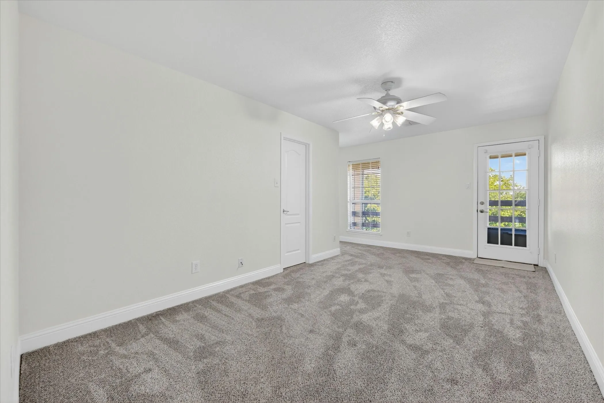 Upstairs Bedroom two Neutral-toned carpeted room featuring a ceiling fan with light fixture, white trim, and a glass-paneled exterior door leading to upstairs balcony
