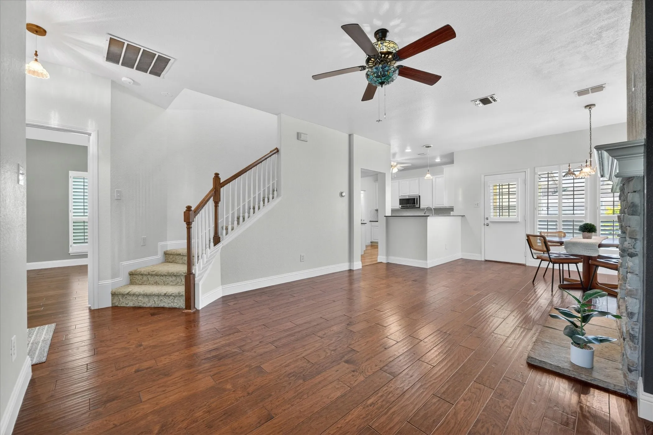 Expansive living area featuring wood-finish flooring, a contemporary ceiling fan, and a stone-clad fireplace