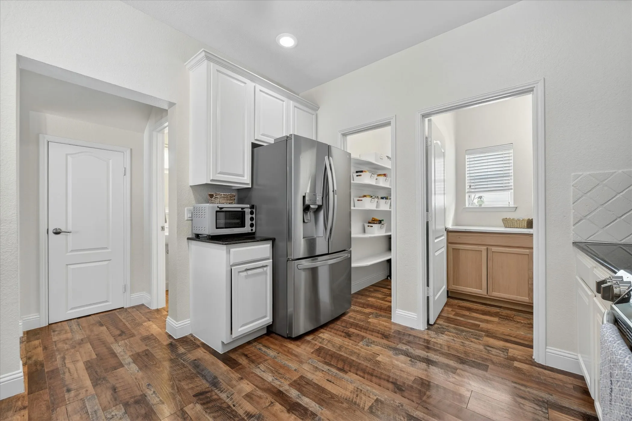 Kitchen featuring wood-finish flooring, white cabinetry, and stainless steel refrigerator
