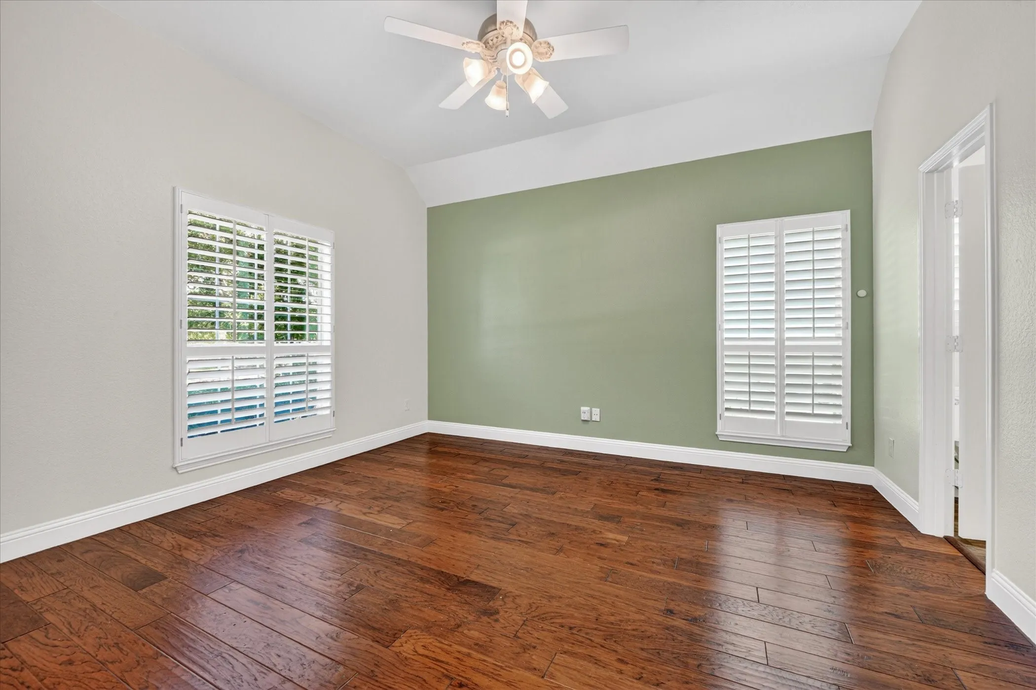 Hardwood flooring throughout featuring a vaulted ceiling with a ceiling fan plantation shutters