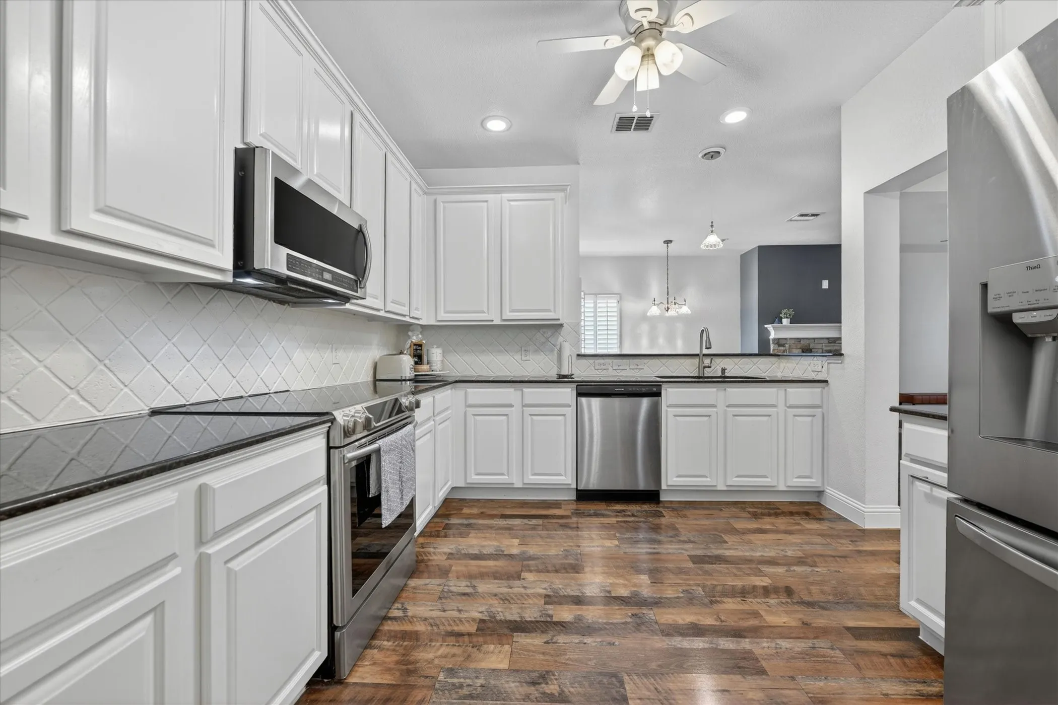 Kitchen featuring white cabinetry, dark countertops, wood-finish flooring, stainless steel appliances, and a tiled backsplash