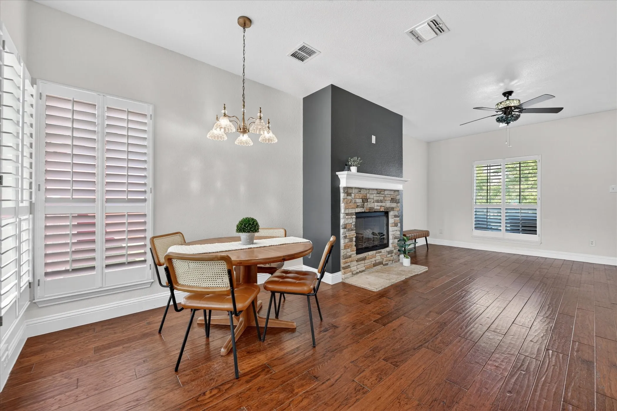 Spacious room with wood-finish flooring, a stone-front fireplace with a mantel, and crisp white plantation shutters