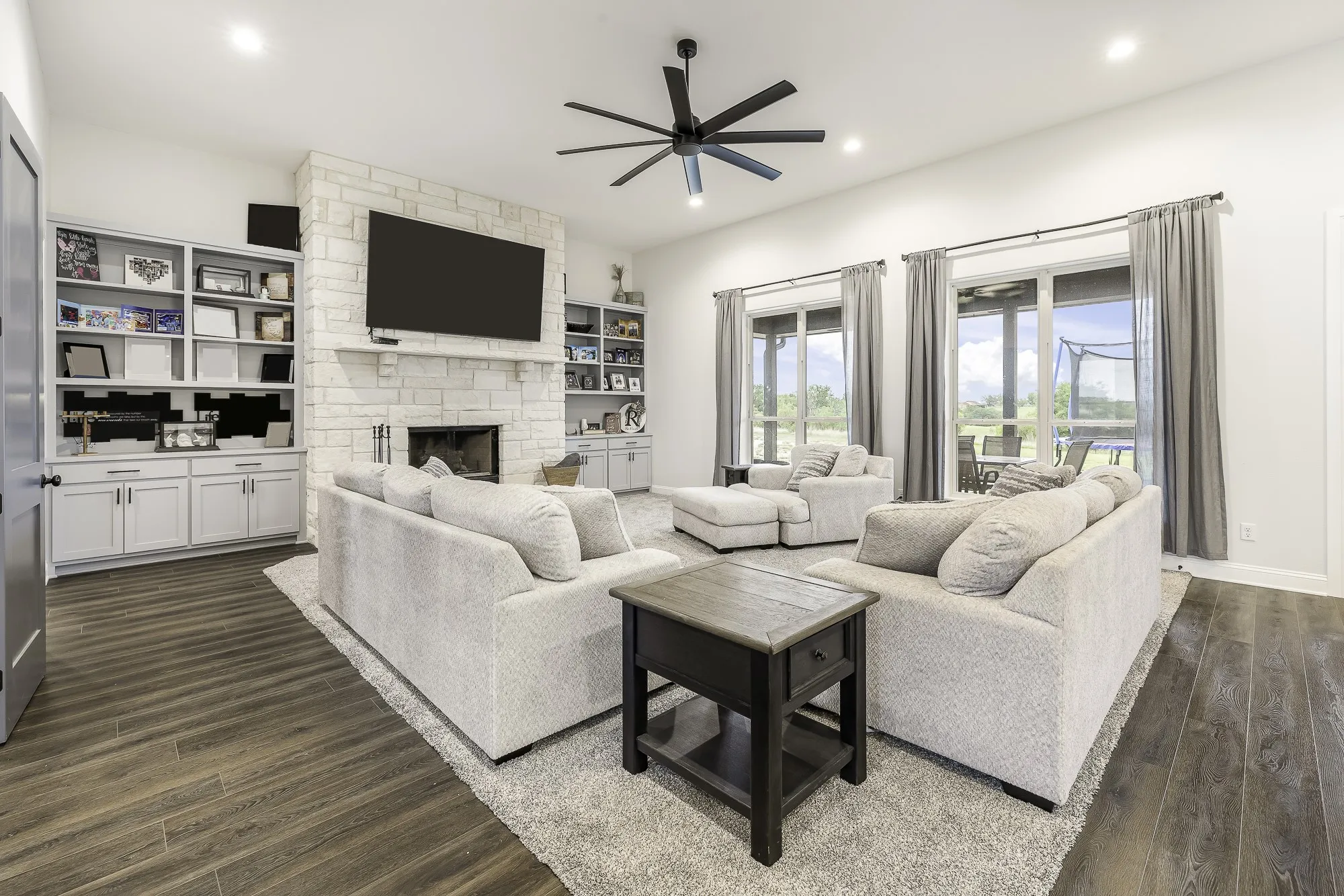 Living area featuring wood-finish flooring, a stone fireplace with a white mantel, and built-in shelving with lower cabinetry