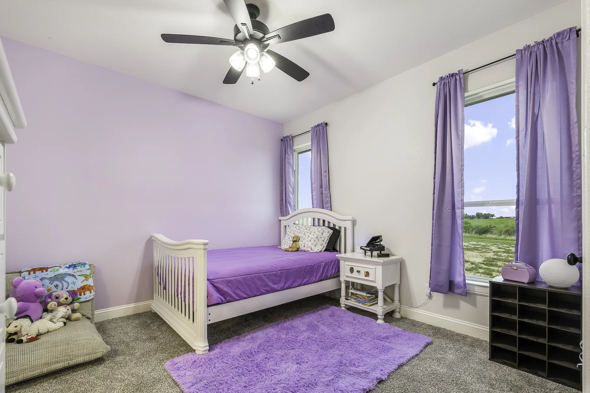 Room featuring soft wall color, carpeted flooring, two windows with draperies, and a ceiling fan with integrated lighting