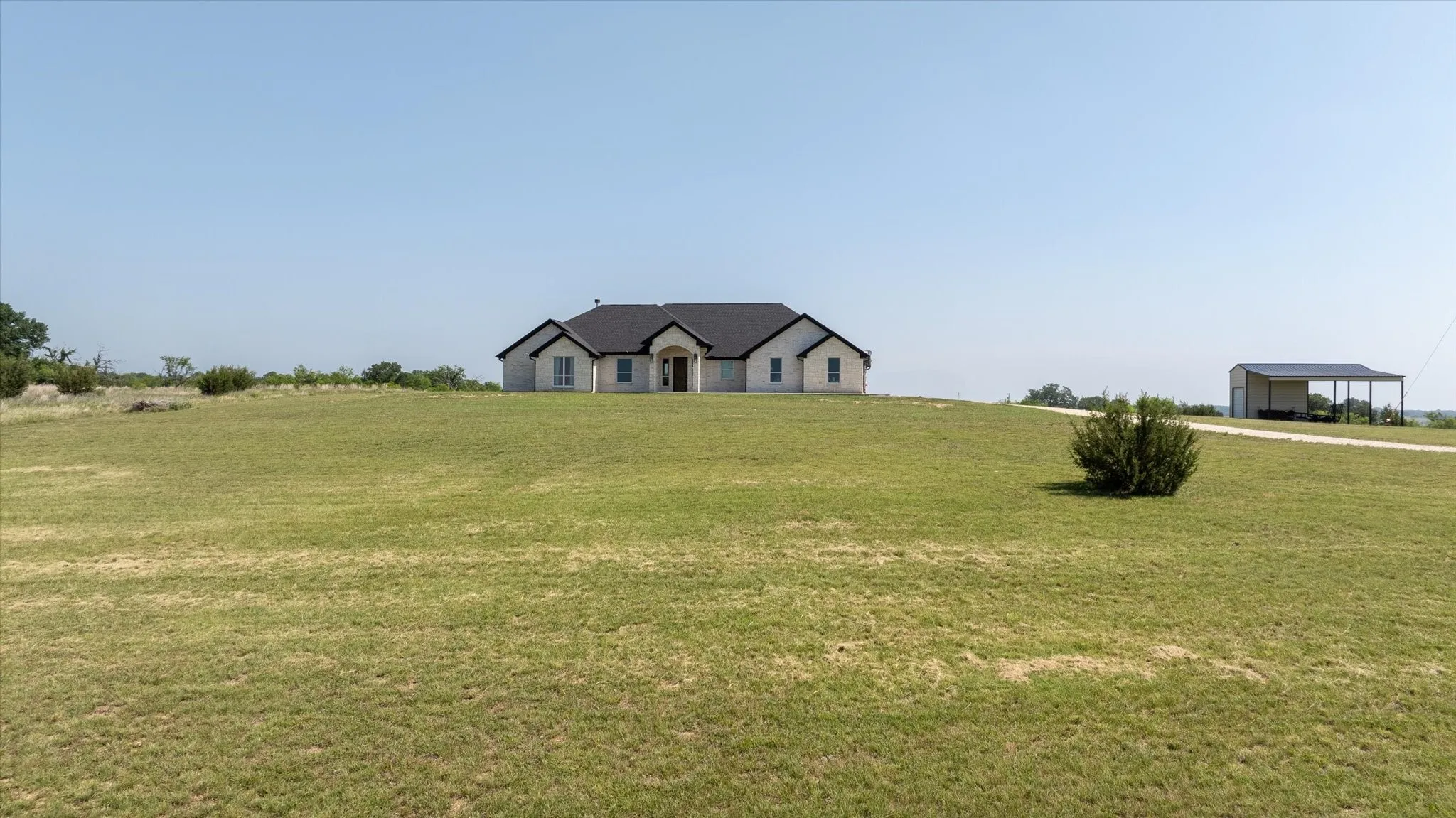 Ranch-style residence featuring a light-colored stone exterior, dark shingle roof, and a covered entry