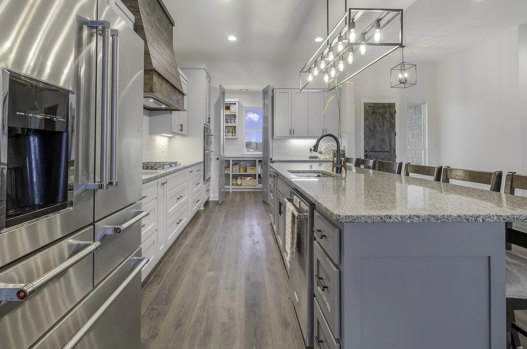 Spacious kitchen featuring an expansive island with granite countertops, stainless steel appliances, wood-finish flooring, white cabinetry, and a designer linear light fixture