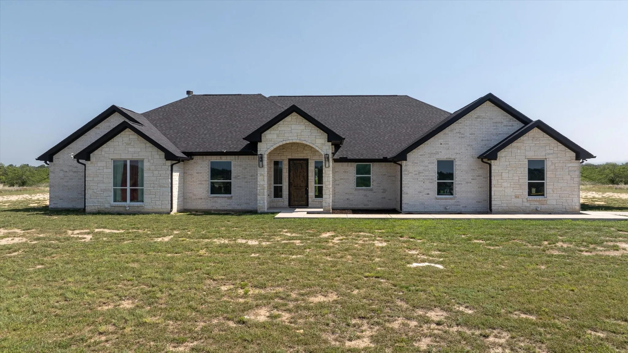 Spacious single-story residence featuring a light-colored stone exterior, a dark shingle roof, and a prominent arched entryway