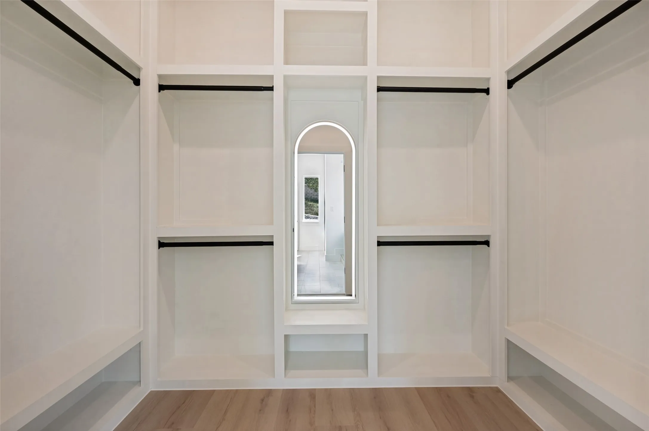 Built-in closet system featuring multiple shelving units, hanging rods, an integrated arch mirror, and wood-finish flooring