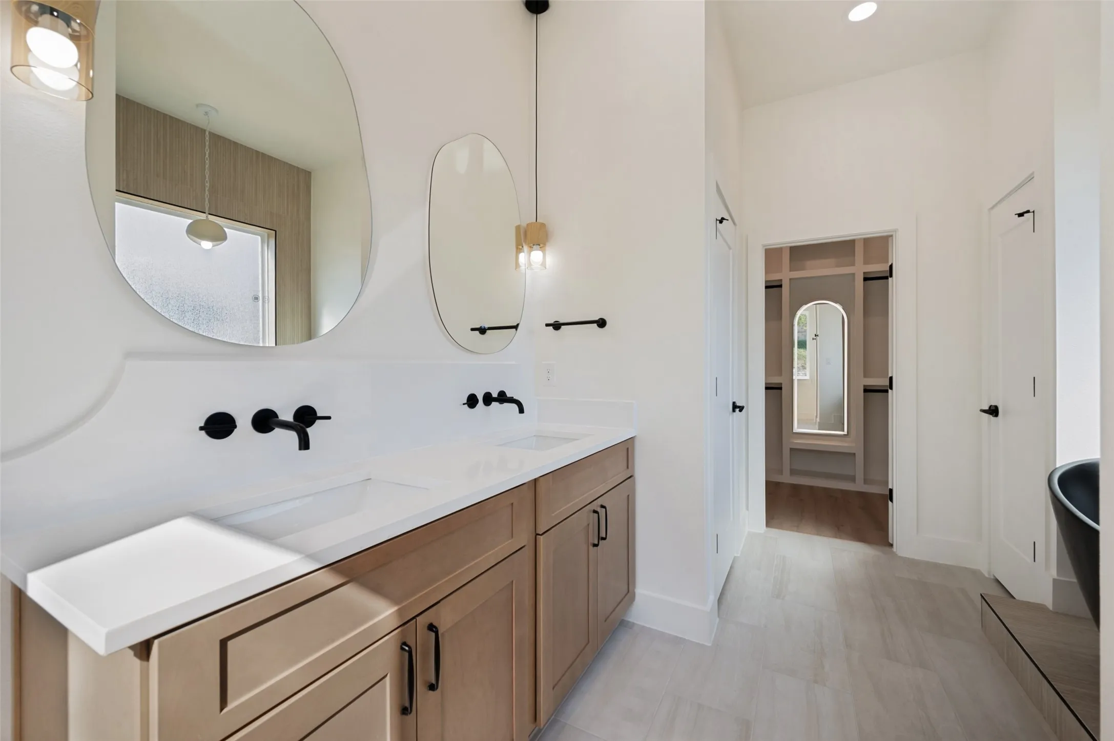 Double vanity featuring light wood-finish cabinetry, white countertops, and wall-mounted matte black faucets