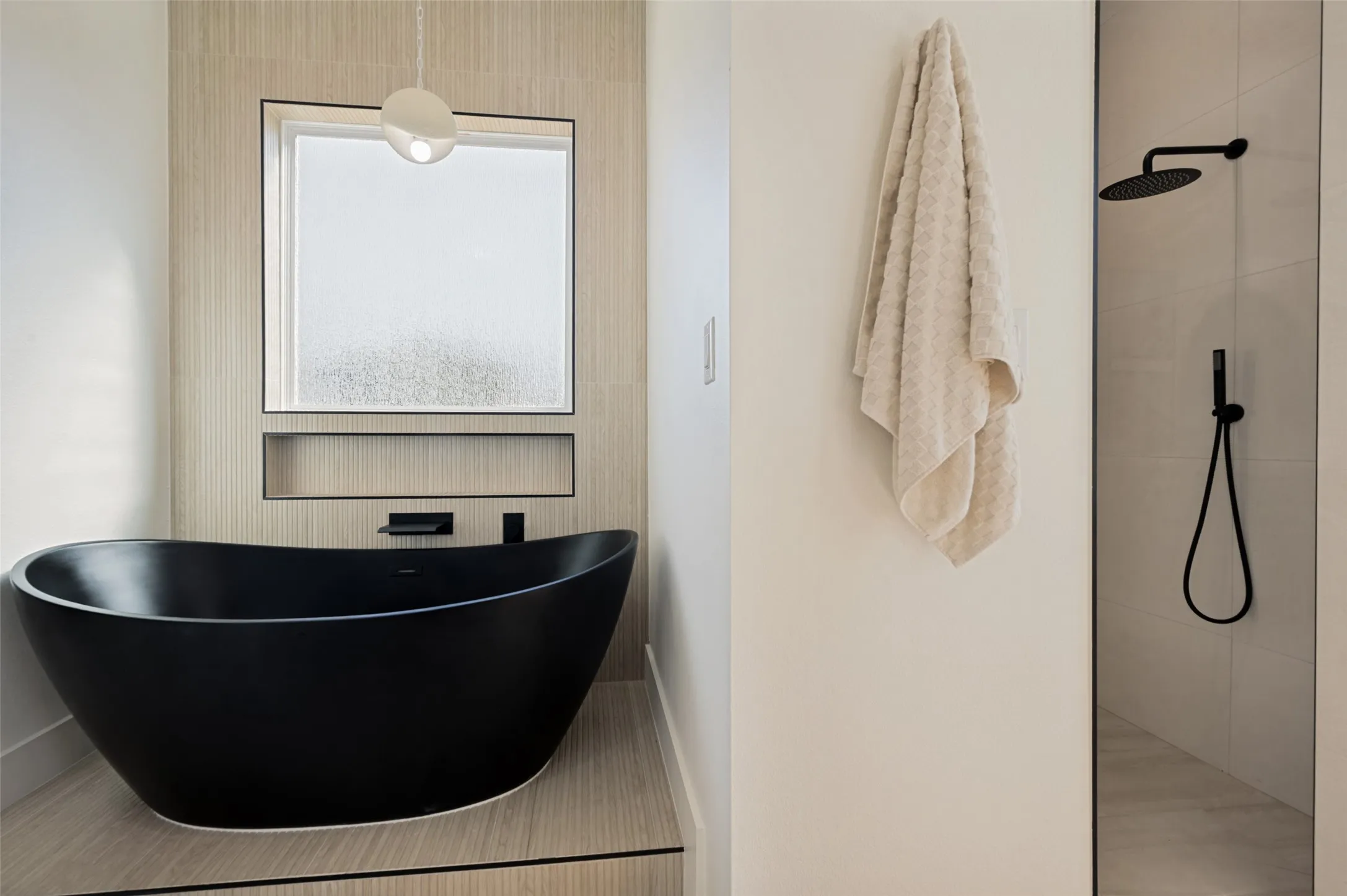 Freestanding black soaking tub with a modern pendant light, recessed shelving, and a frosted window