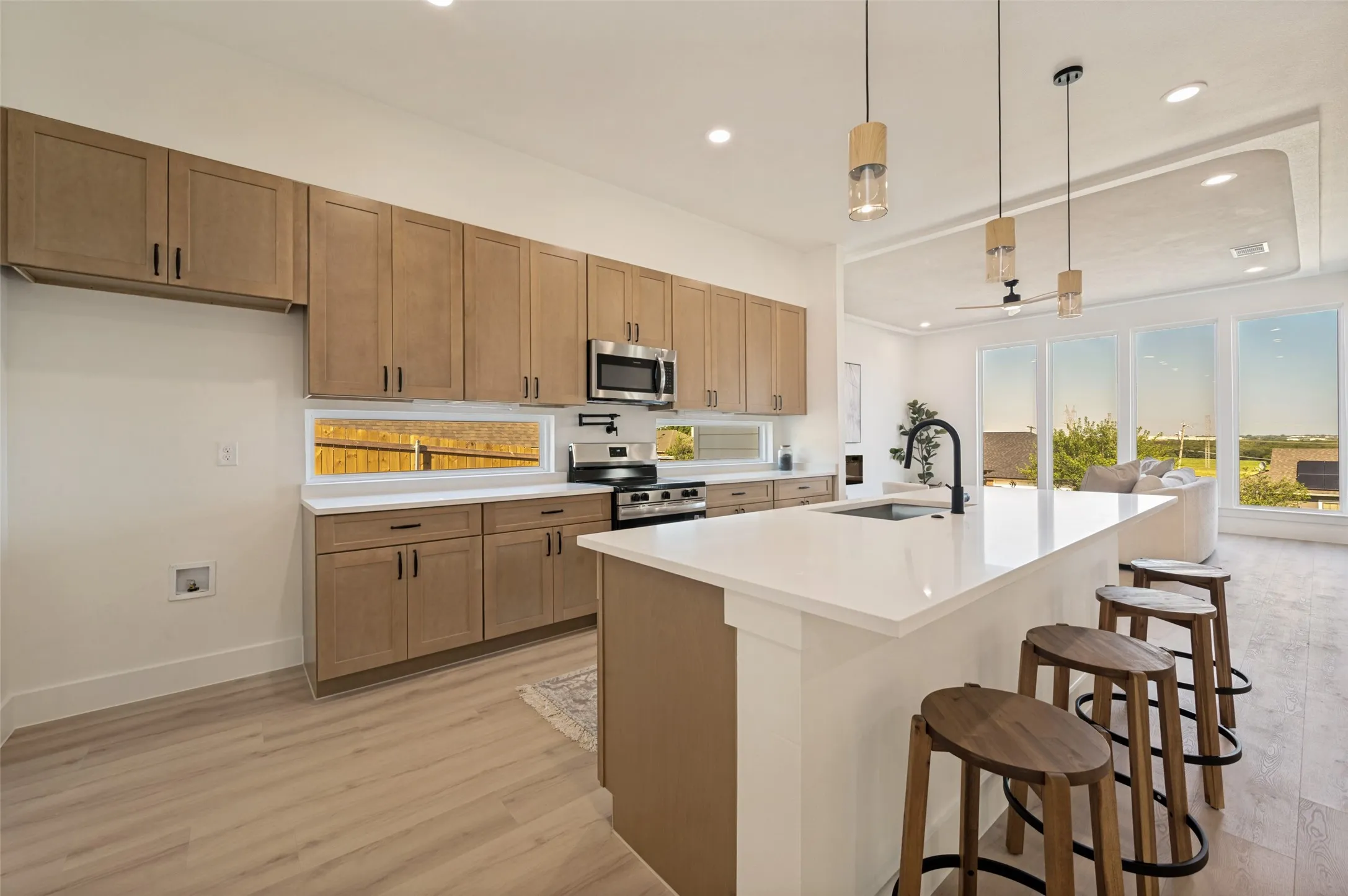 Modern kitchen featuring light wood-finish cabinetry, stainless steel appliances, a white countertop island with seating, recessed lighting, and wood-finish flooring