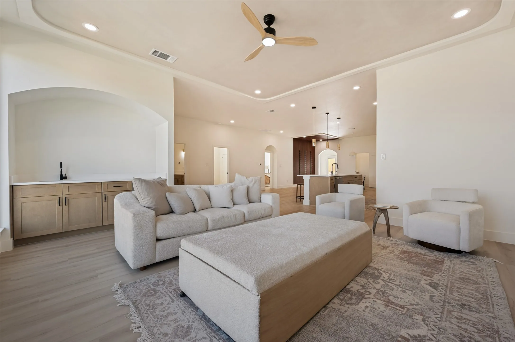 Spacious living area featuring light wood-finish flooring and a tray ceiling with recessed lighting and a ceiling fan