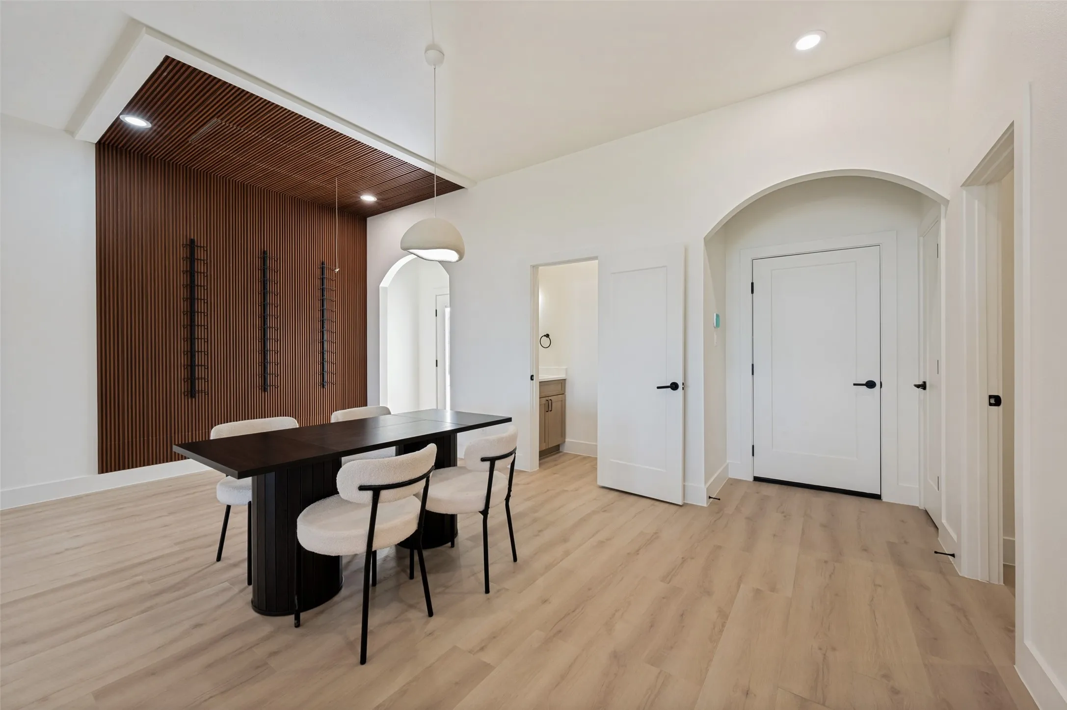 Open-concept room featuring a striking wood-slat accent wall, light wood-finish flooring, and vaulted white ceilings