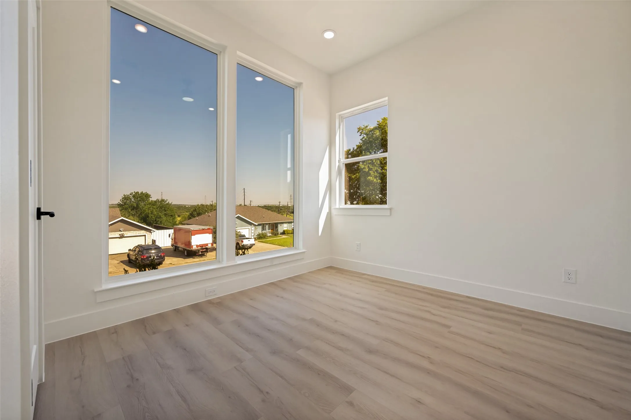 Light-filled interior space featuring two tall picture windows, an additional casement window, recessed ceiling lighting, and wood-finish flooring