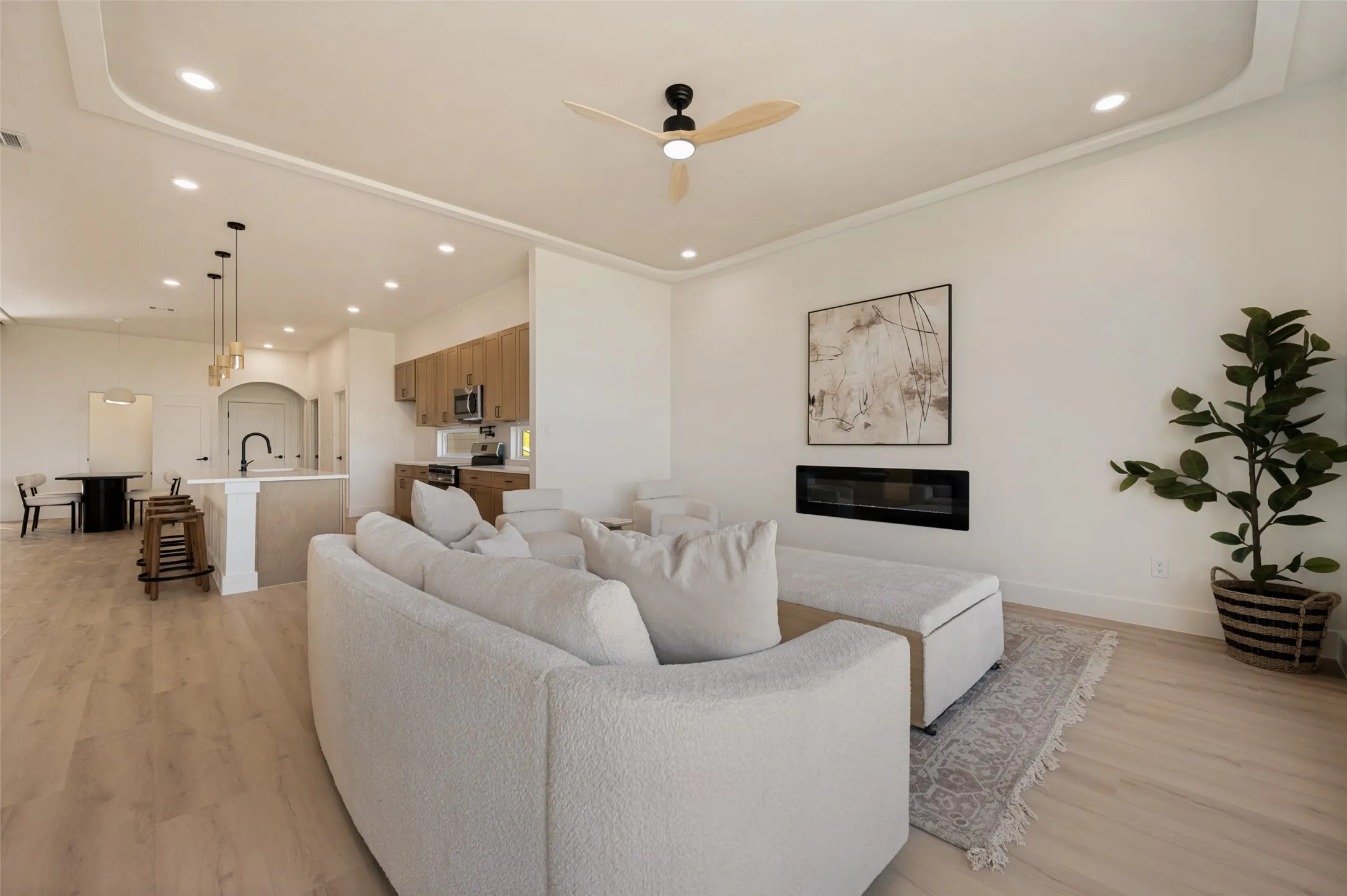 Spacious living area featuring light wood-finish flooring, recessed lighting, and a modern linear fireplace
