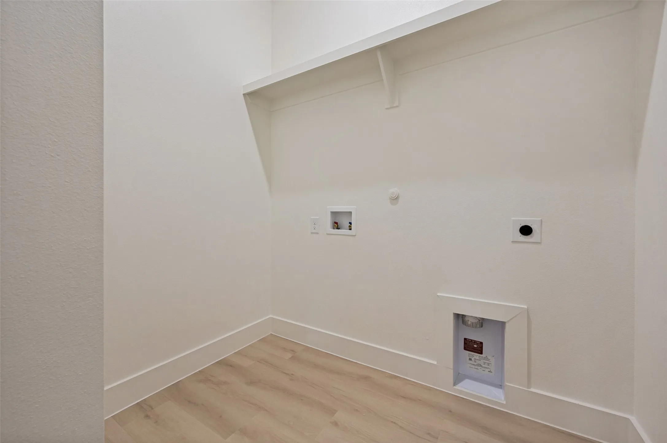 Laundry area featuring wood-finish flooring, white walls, and a built-in shelf