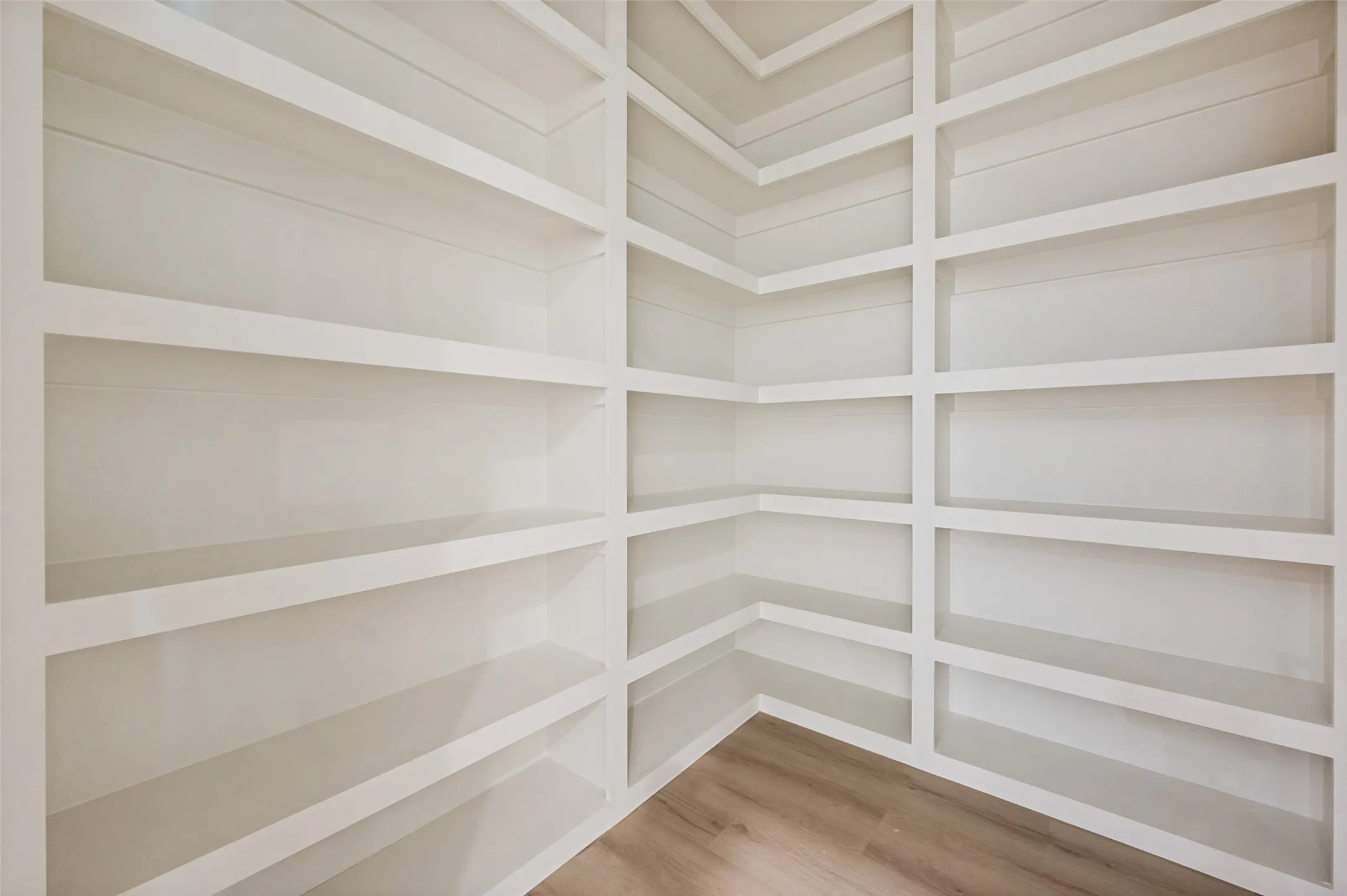 Built-in shelving with multiple storage compartments, white painted finish, and wood-finish flooring