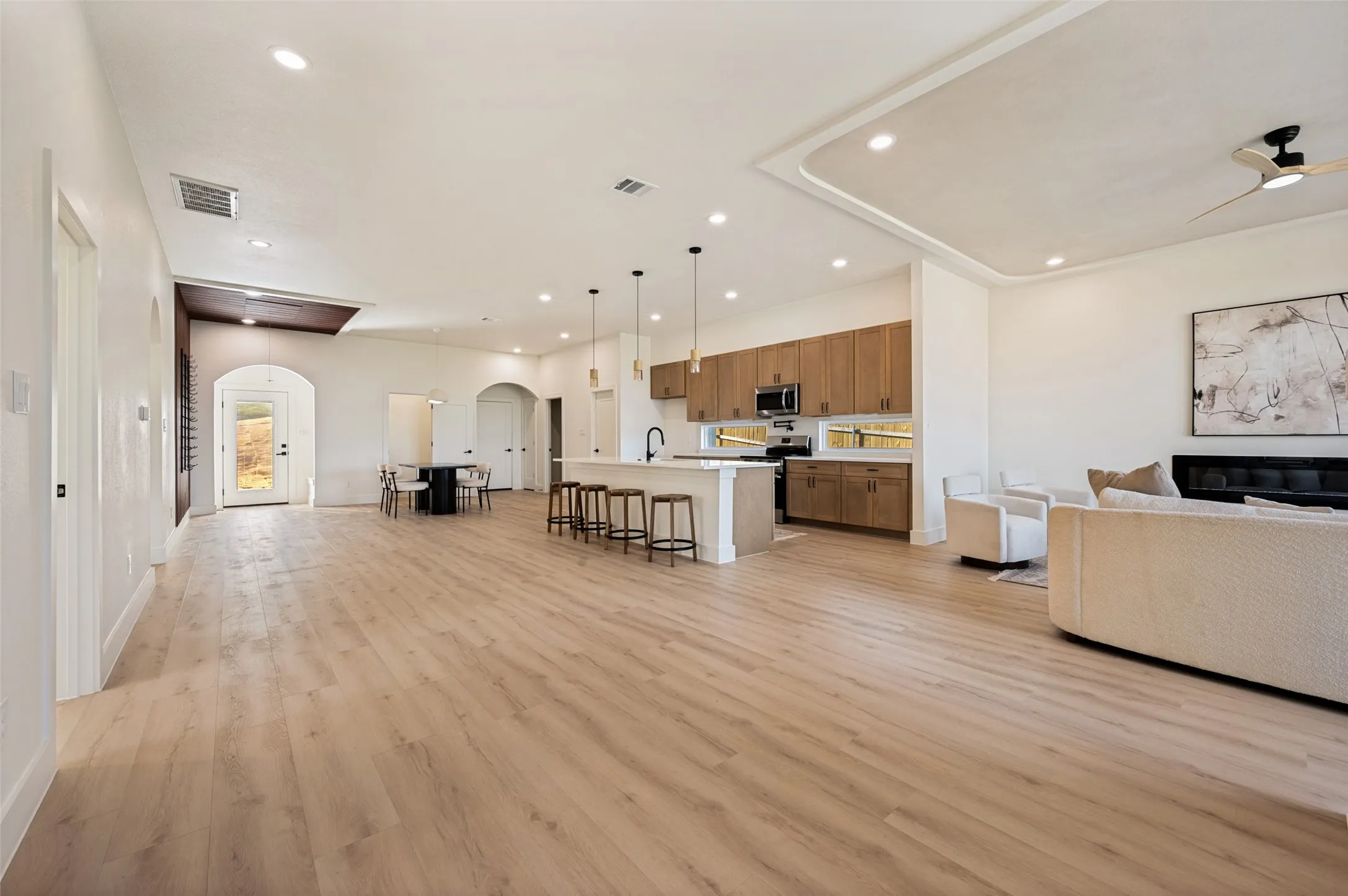 Expansive open-concept space featuring light wood-finish flooring, recessed lighting, and a tray ceiling