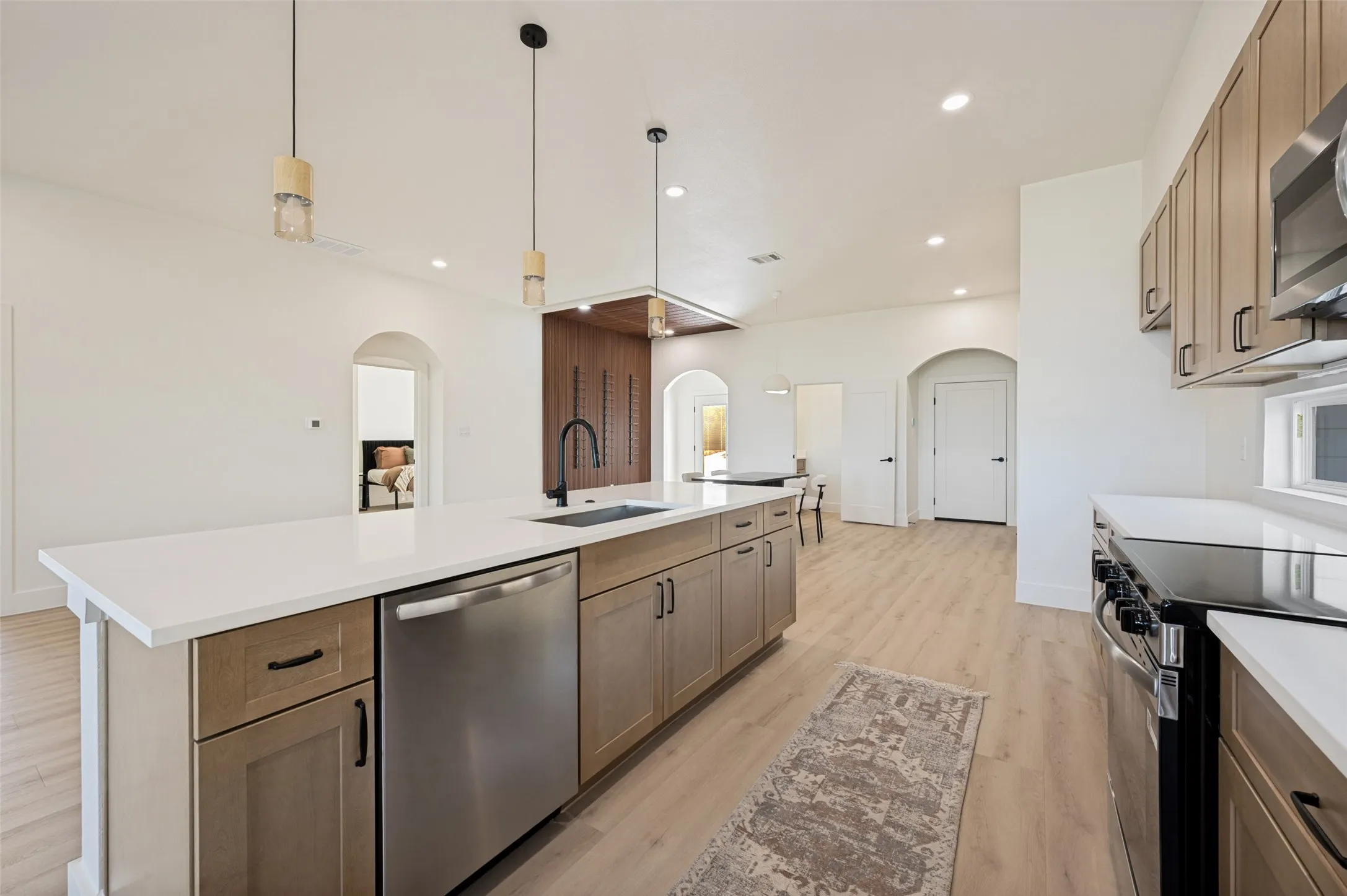 Modern kitchen featuring a large island with white countertops, integrated stainless steel appliances, and wood-finish cabinetry