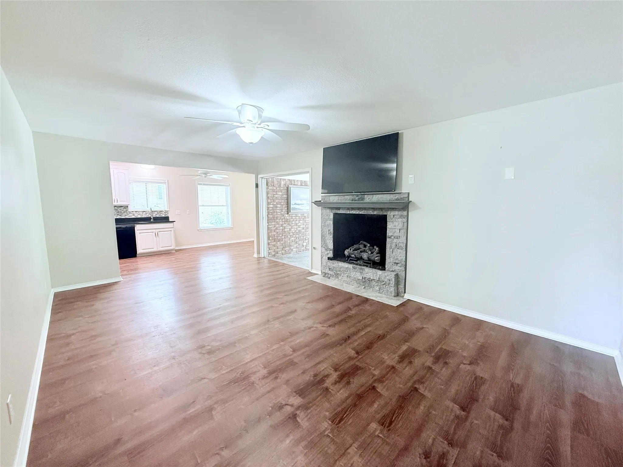Spacious living area featuring wood-finish flooring, a stone-clad fireplace, and a ceiling fan