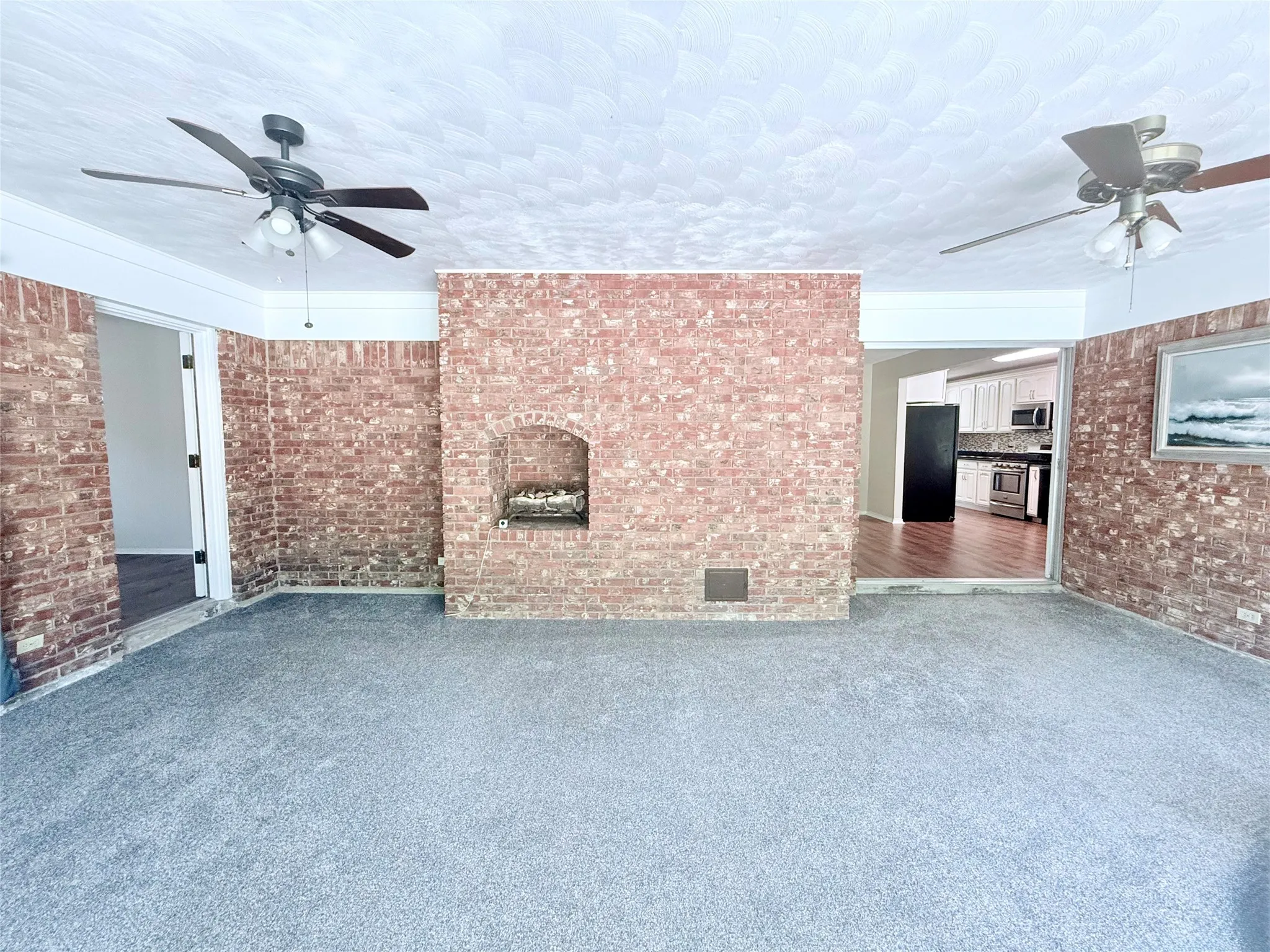 Living area featuring brick accent walls, a built-in fireplace, and two ceiling fans