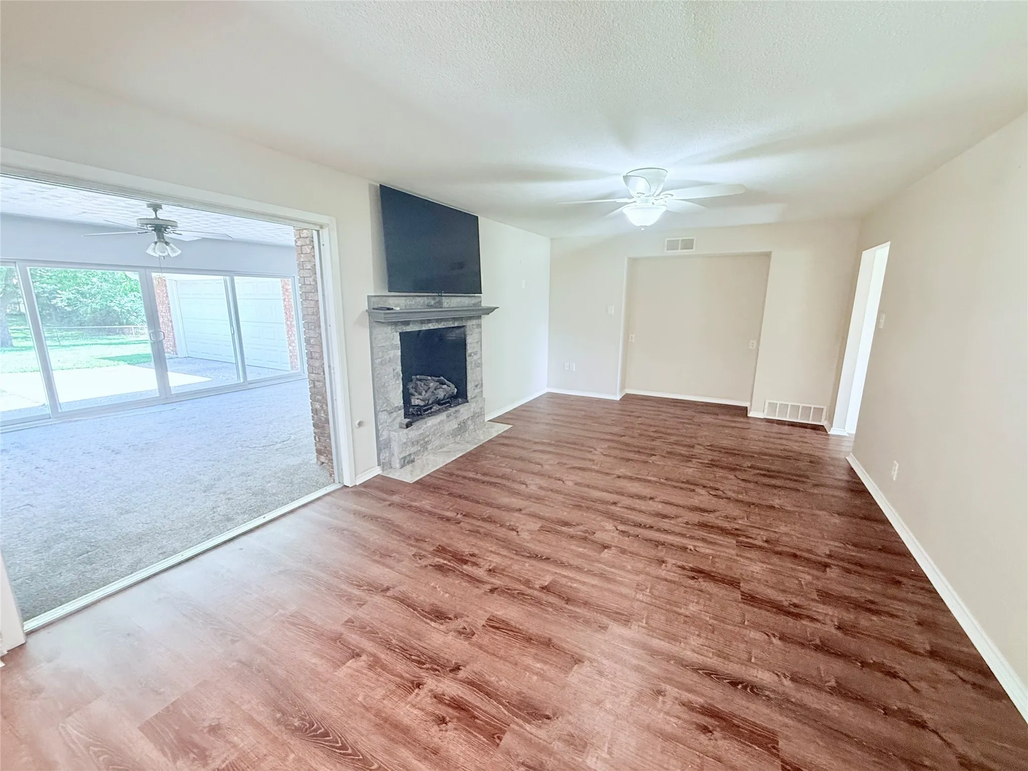Spacious living area featuring wood-finish flooring, a contemporary fireplace with a stone surround, and an overhead ceiling fan