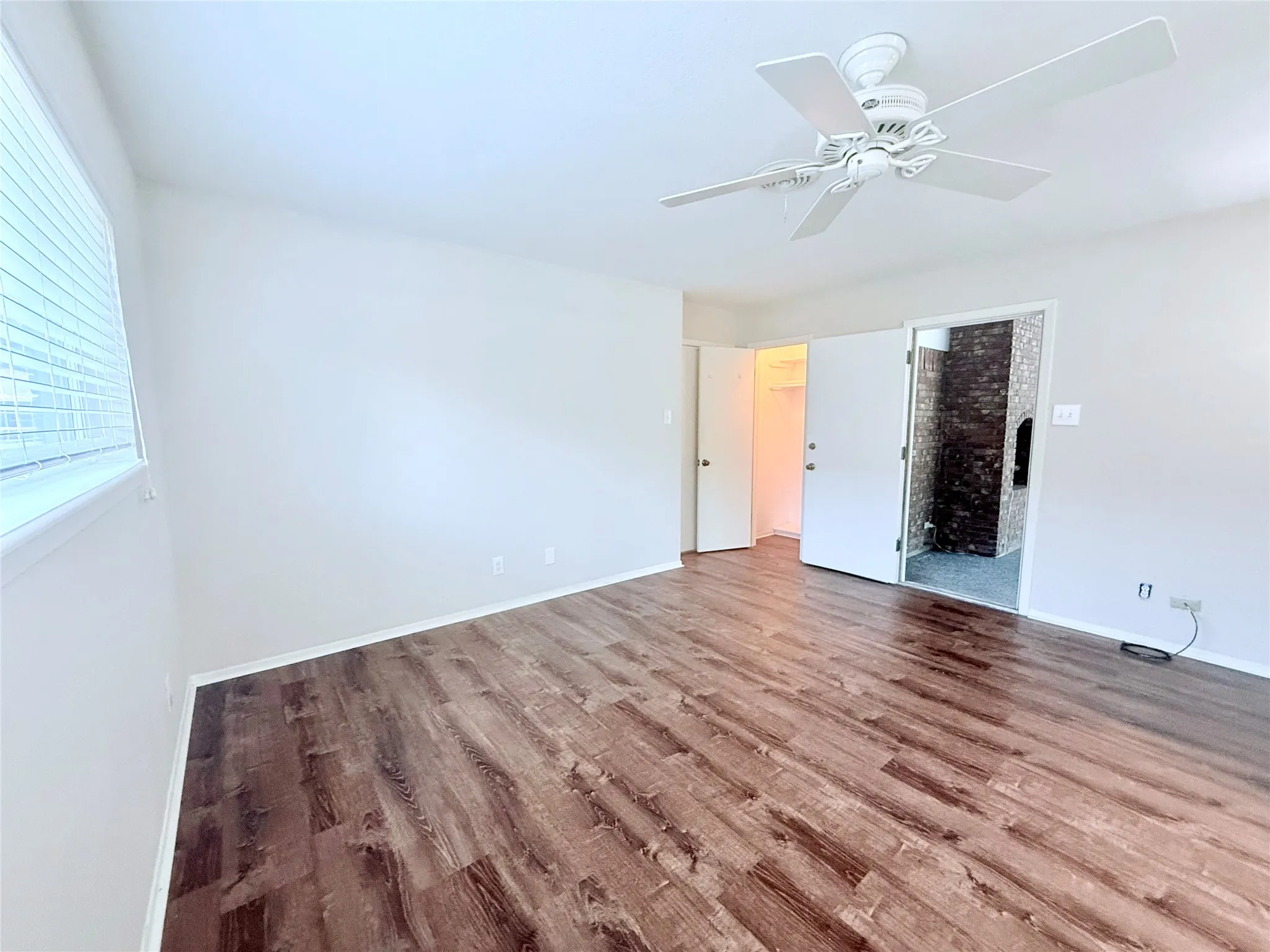 Spacious room featuring wood-finish flooring, light-toned walls, and a ceiling fan