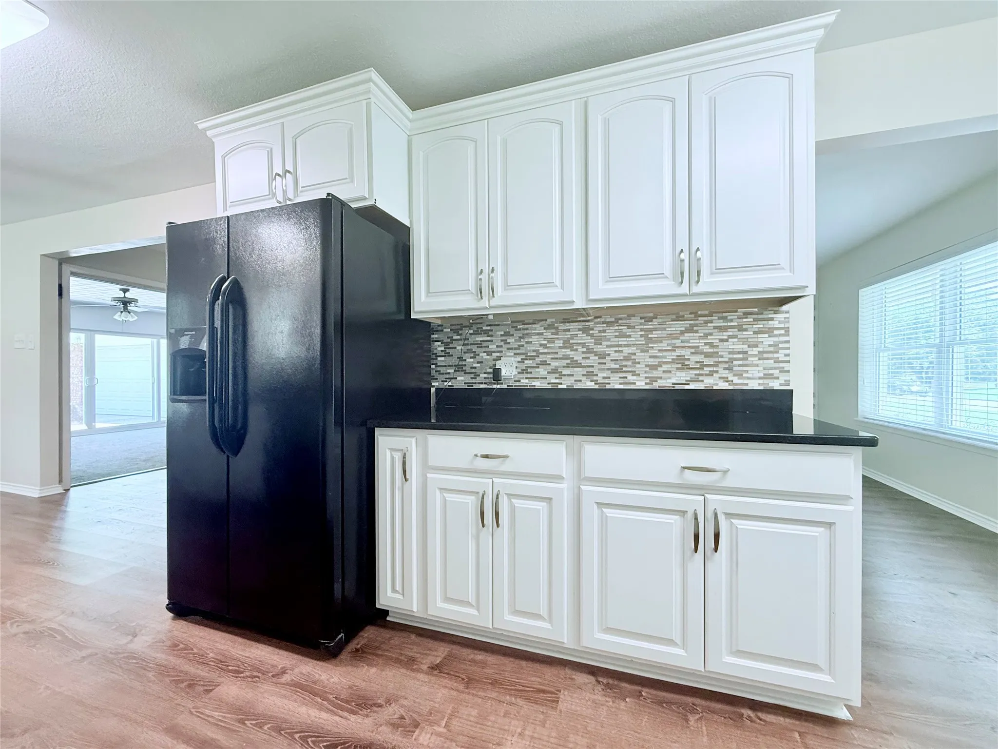 Kitchenette featuring white cabinetry with brushed nickel hardware, a black countertop, and a mosaic tile backsplash