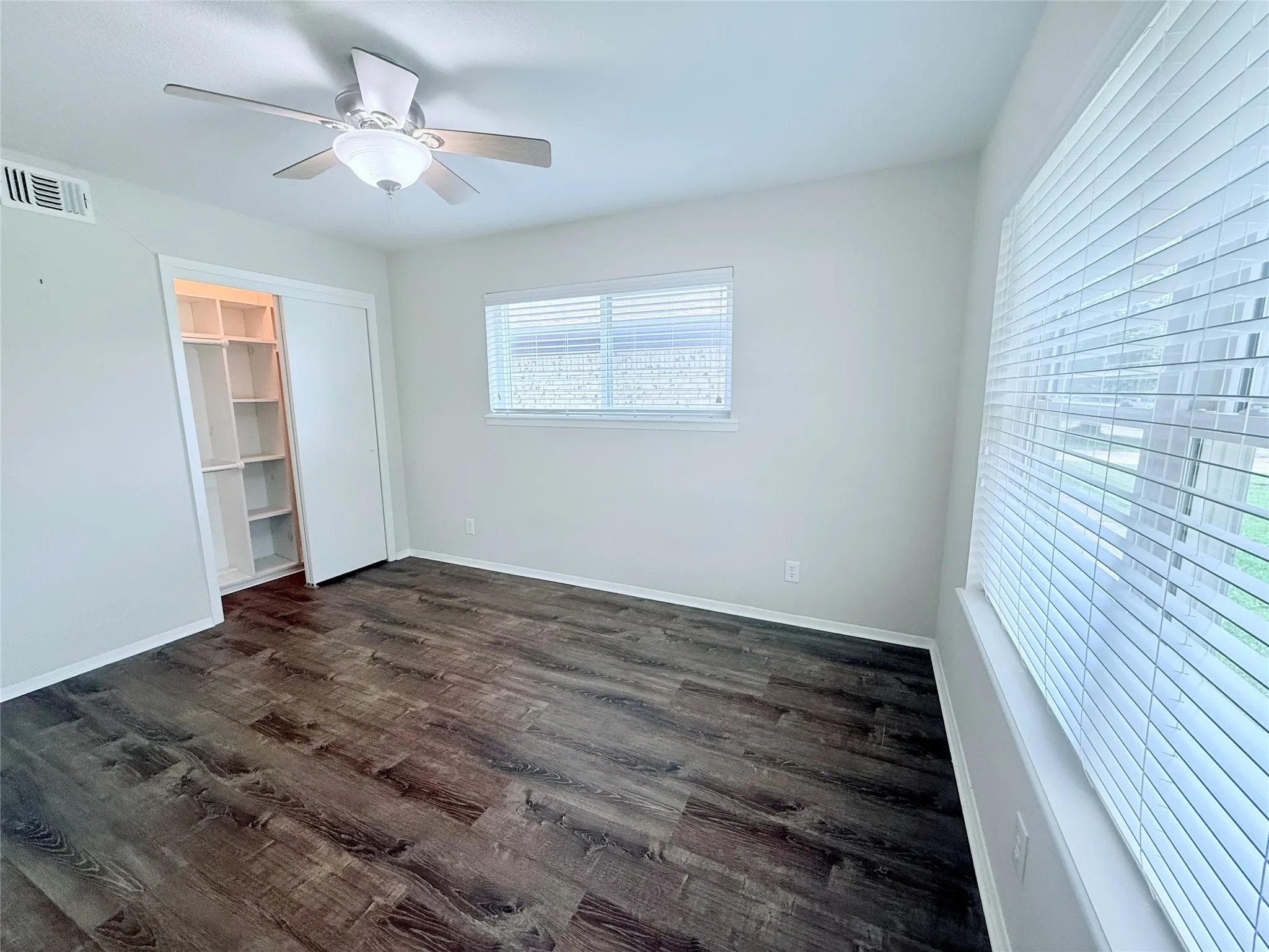 Spacious room featuring wood-finish flooring, light grey walls, and two windows with white blinds