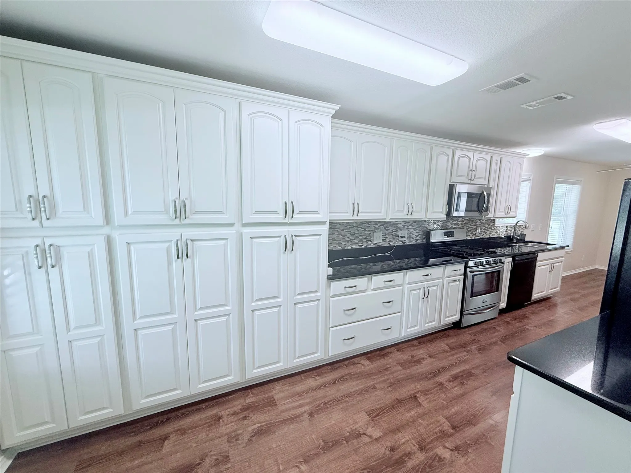 Expansive kitchen featuring abundant white cabinetry, dark countertops, a mosaic tile backsplash, stainless steel appliances, and wood-finish flooring