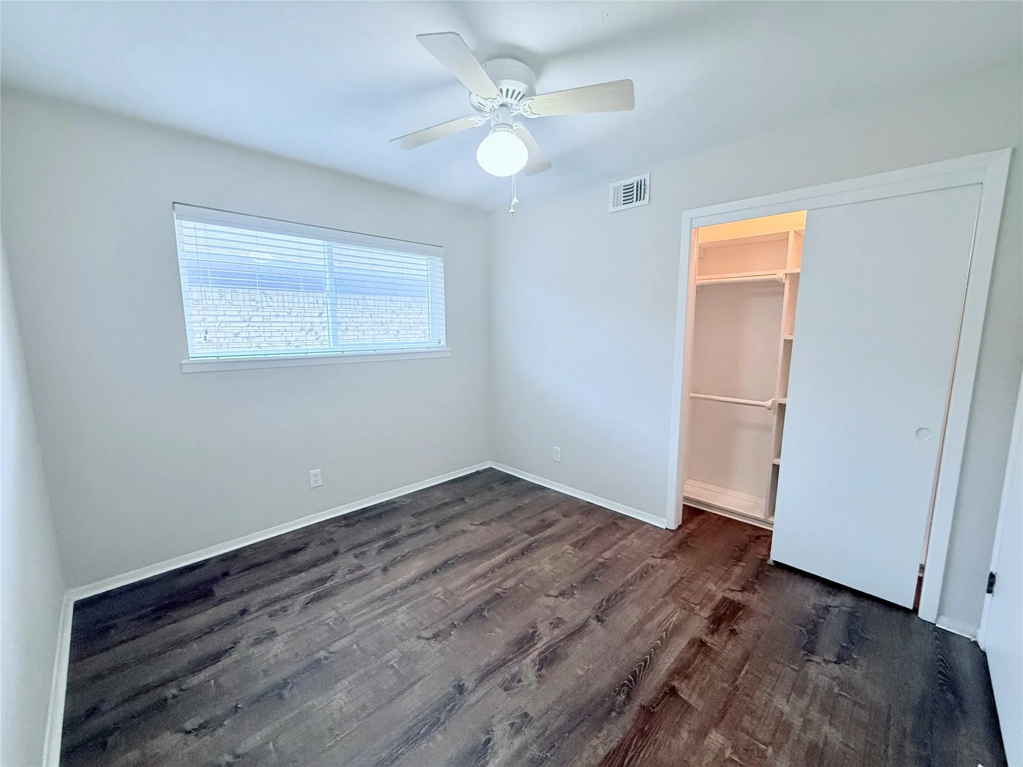 Spacious room featuring wood-finish flooring, a ceiling fan with integrated lighting, and a window with horizontal blinds