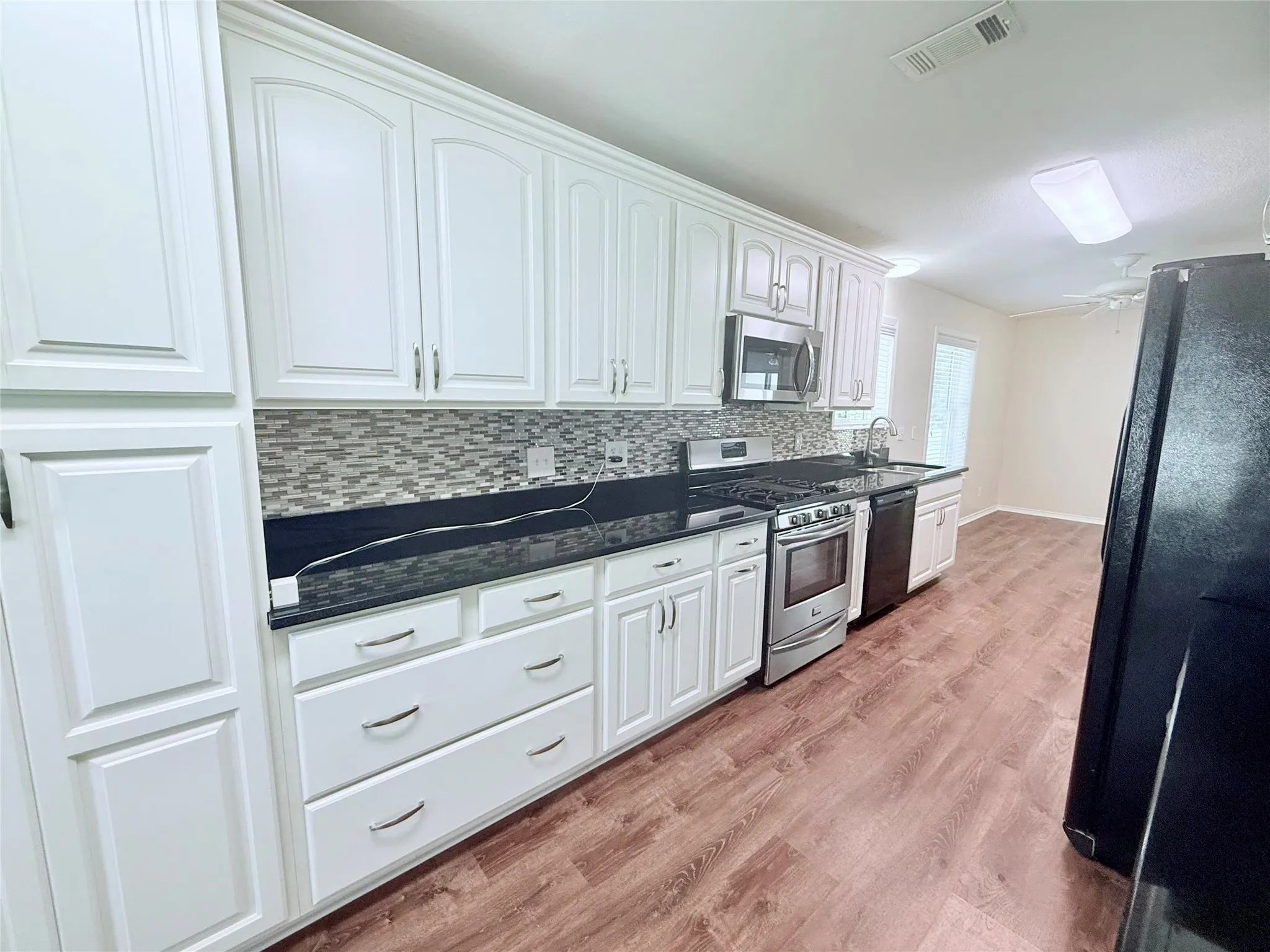 Kitchen featuring white shaker-style cabinetry with chrome hardware, dark countertops, stainless steel appliances, and a mosaic tile backsplash