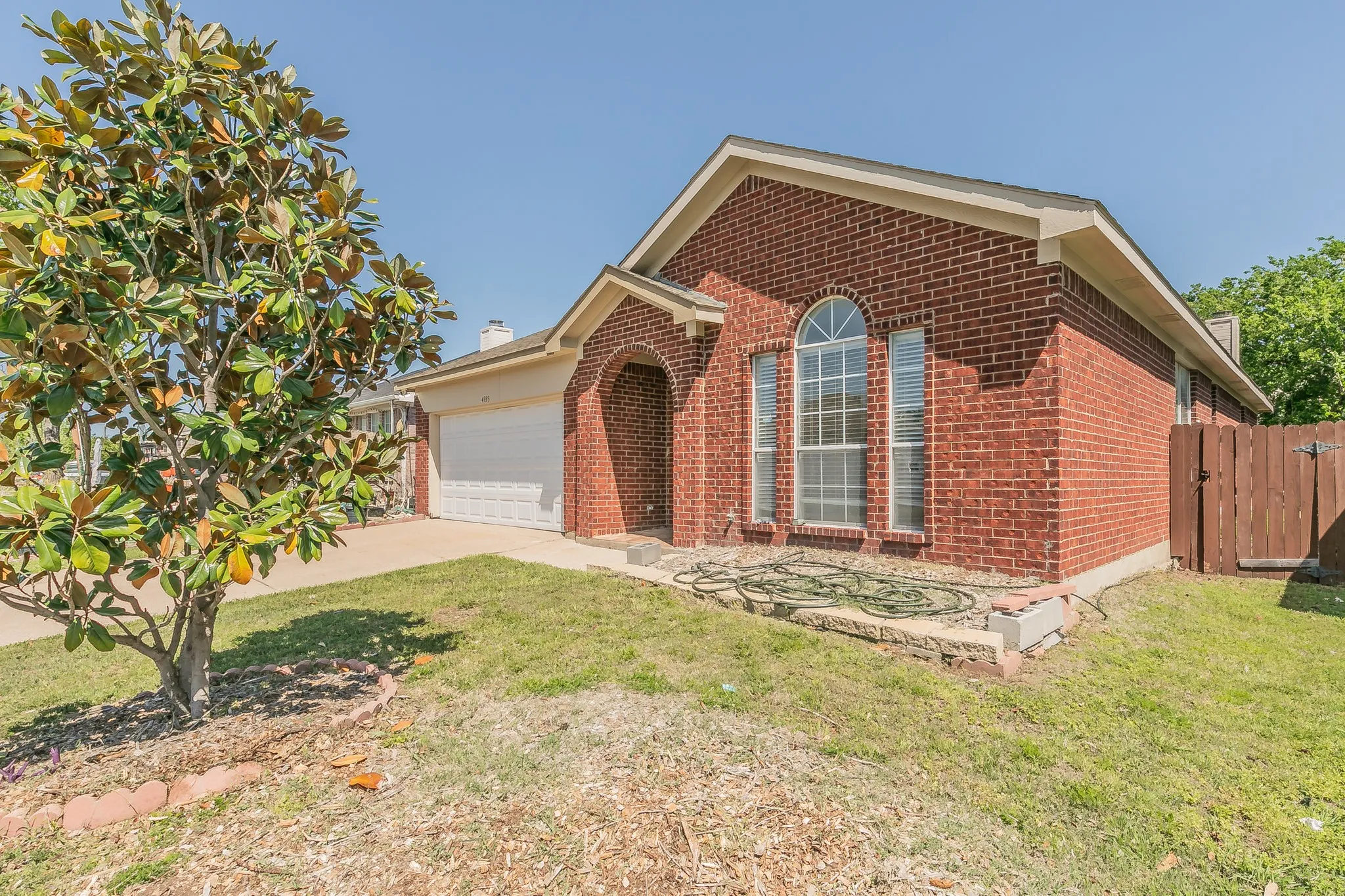 Ranch-style home featuring a front yard, an attached garage, fence, brick siding, and driveway