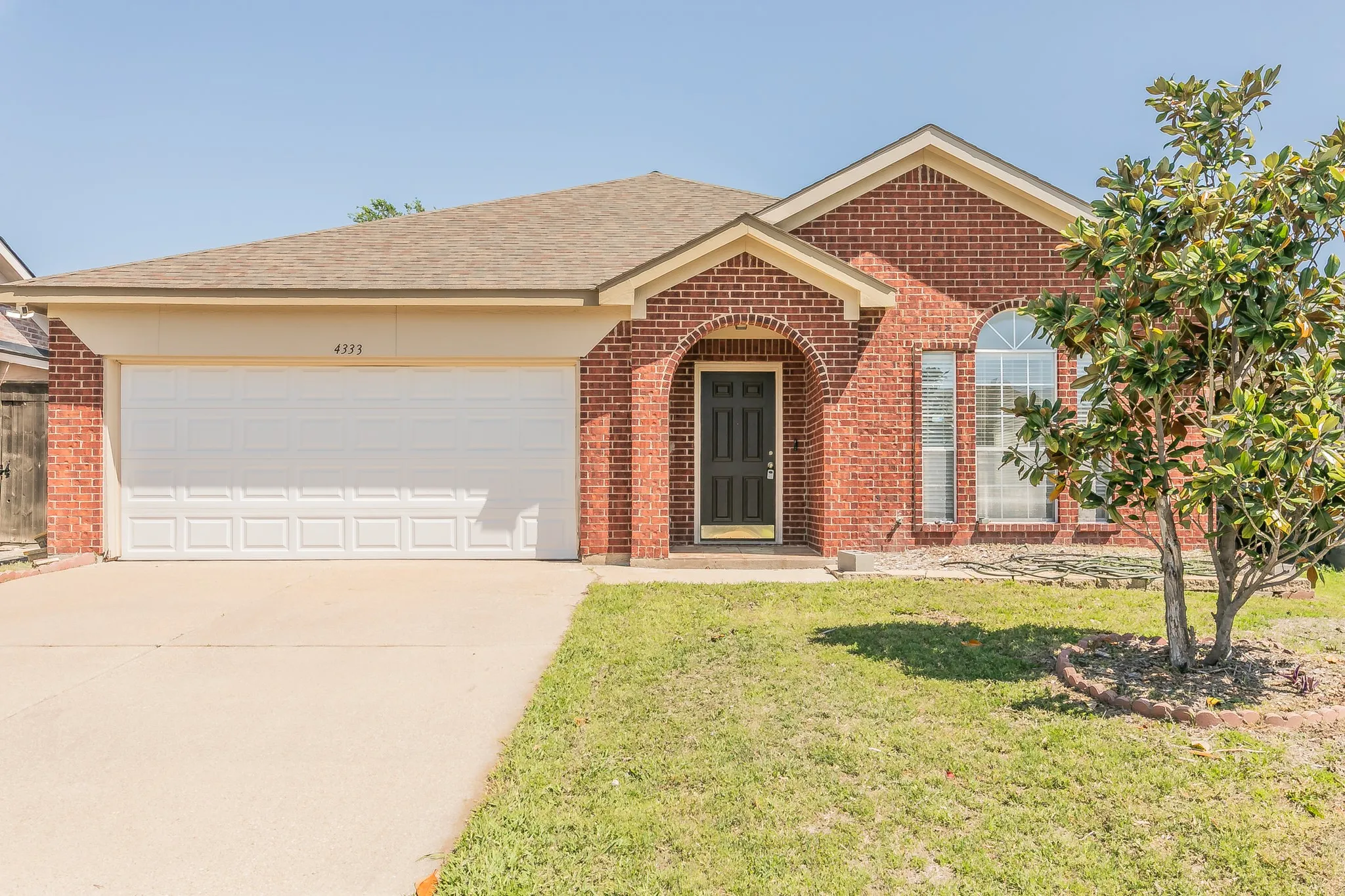 Ranch-style house featuring a garage, a front yard, brick siding, and driveway